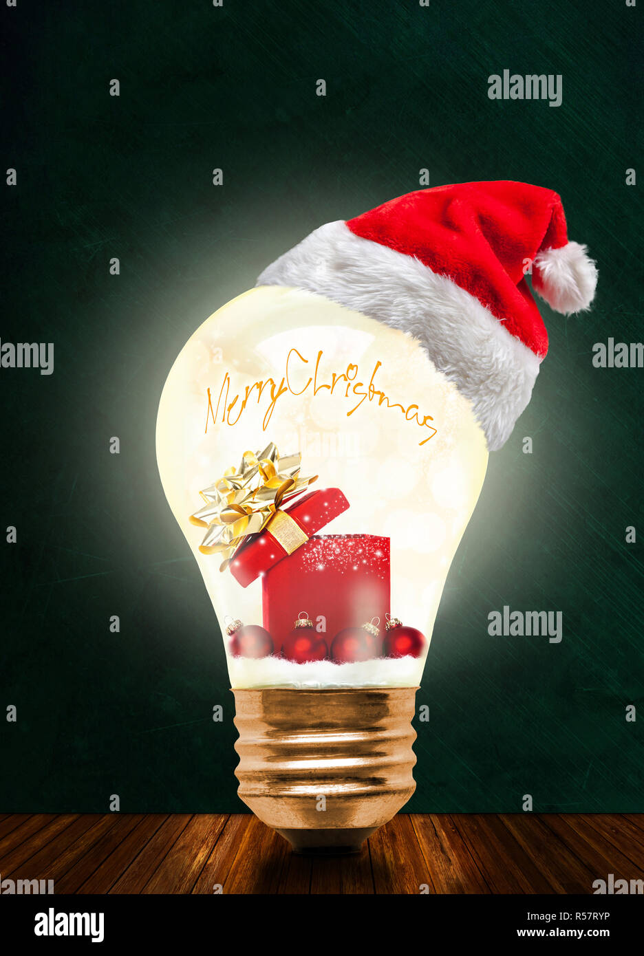 Glowing light bulb wearing Santa hat with Merry Christmas message and magical gift box and baubles with copy space. Glowing Xmas and season of sharing Stock Photo