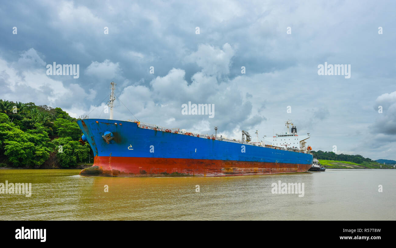 A large cargo ship makes its way through the Panama Canal waterways,  Each side between lift locks is flanked with green rainforest jungle. Stock Photo