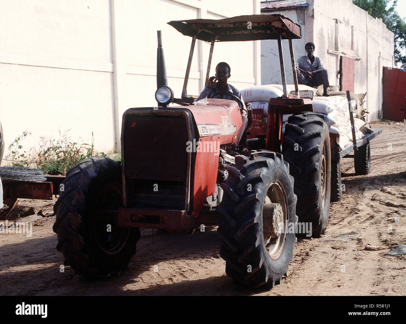 1993 - A Somali man drives a tractor pulling a trailer full of supplies at the food storage warehouse in Kismayo.  After the food is accounted for, it is delivered to food distribution centers throughout the city by United Nations Forces in Somalia in support of  OPERATION CONTINUE HOPE. Stock Photo