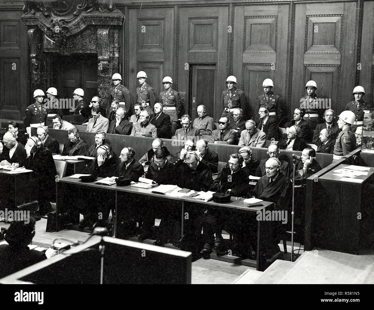 The prosecution charges the defendants with conspiring to destroy the independence of other nations. Goering is in the defendant's box. The defendants, surrounded by American military police, Goering, Hess, Von Ribbentrop, Keiter, Rosenberg, Frank, Frick, Streicher, Funk, Schacht; back row, Donitz, Raeder, Von Schirach, Sauckel, Jodl, Von Papen, Seyss-Inquart, Speer, Von Neurath, and Hans Fritsche. 11/23/45. Stock Photo