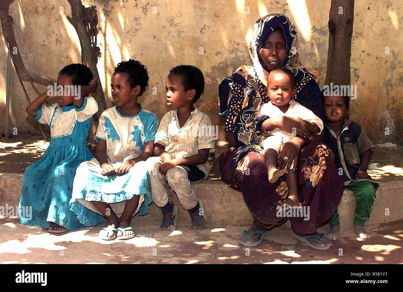 1993 - Straight on shot of five Somali children and a Somali woman as they sit on a curb waiting patiently for their turn to see US Navy doctors conducting a medical civic action program in the capital city of Mogadishu, Somalia. Stock Photo