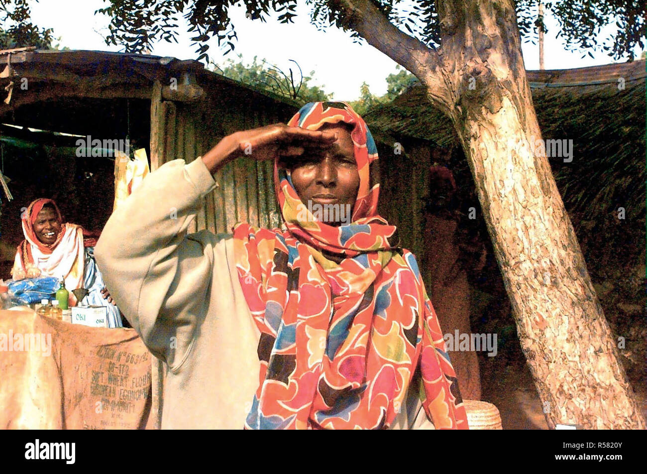 1993 - Straight on shot of a Somali woman from the waist up as she renders a salute to show her support for American Forces (not shown) in Somalia in support of Operation Continue Hope.  The photograph was taken in the market area of Kismayo, Somalia.  Another Somali woman is seen at the left in the background and she's laughing. Stock Photo