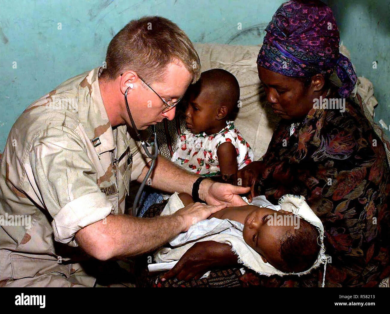1993 - A US Navy doctor examines a Somali infant in her mother's arms during a medical civic action program in the capital city of Mogadishu, Somalia. Stock Photo
