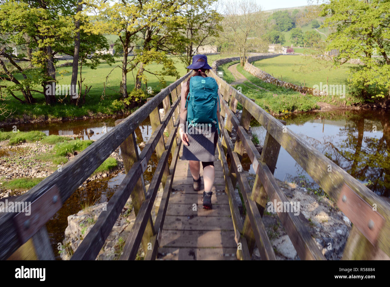 A young female hiker walking along a footbridge over the river Wharfe, near Starbotton, in the Yorkshire Dales Way, Northern England, United Kingdom. Stock Photo