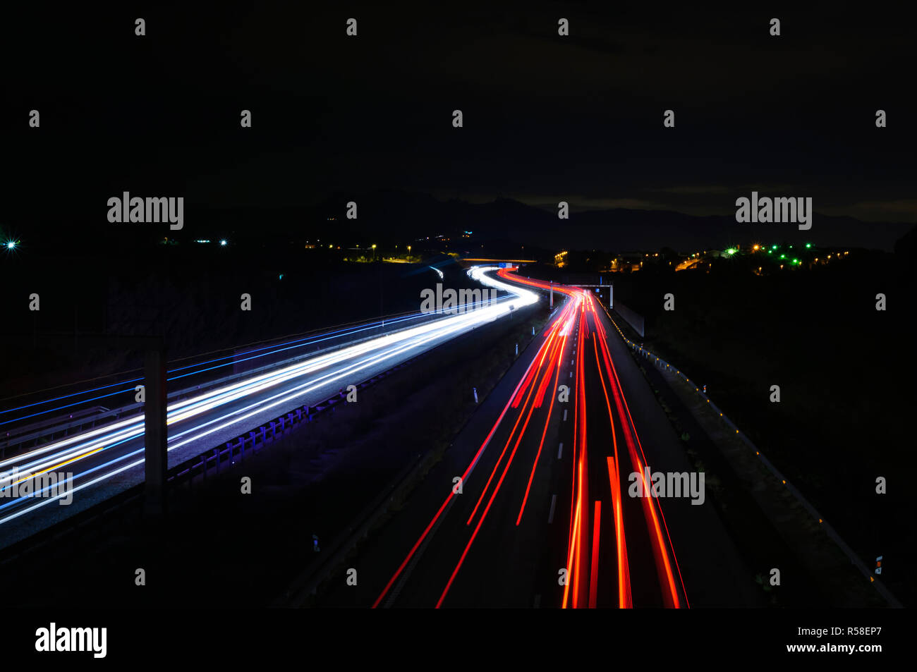 Car trails at night along a road and a city on the background Stock Photo