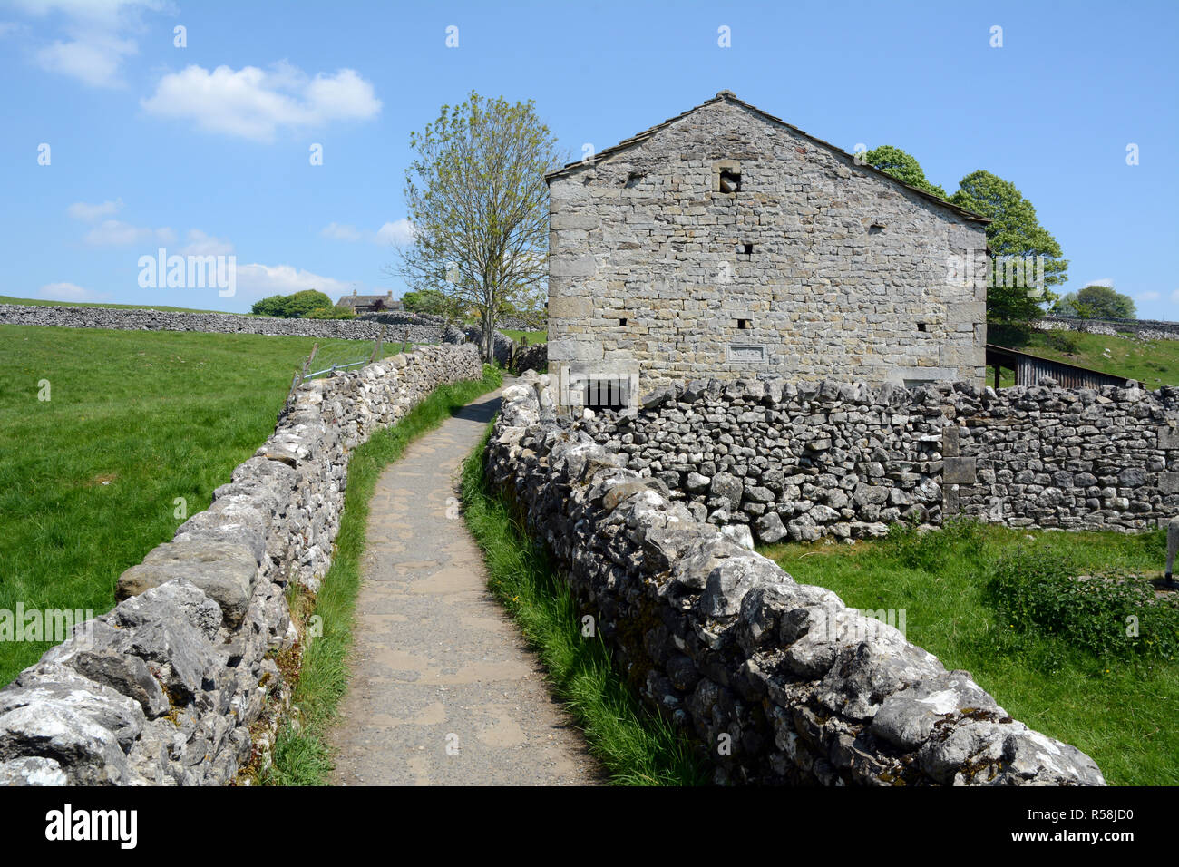 A gravel footpath running between dry stone walls and beside a cottage along The Dales Way hiking trail, in Yorkshire, England, United Kingdom. Stock Photo