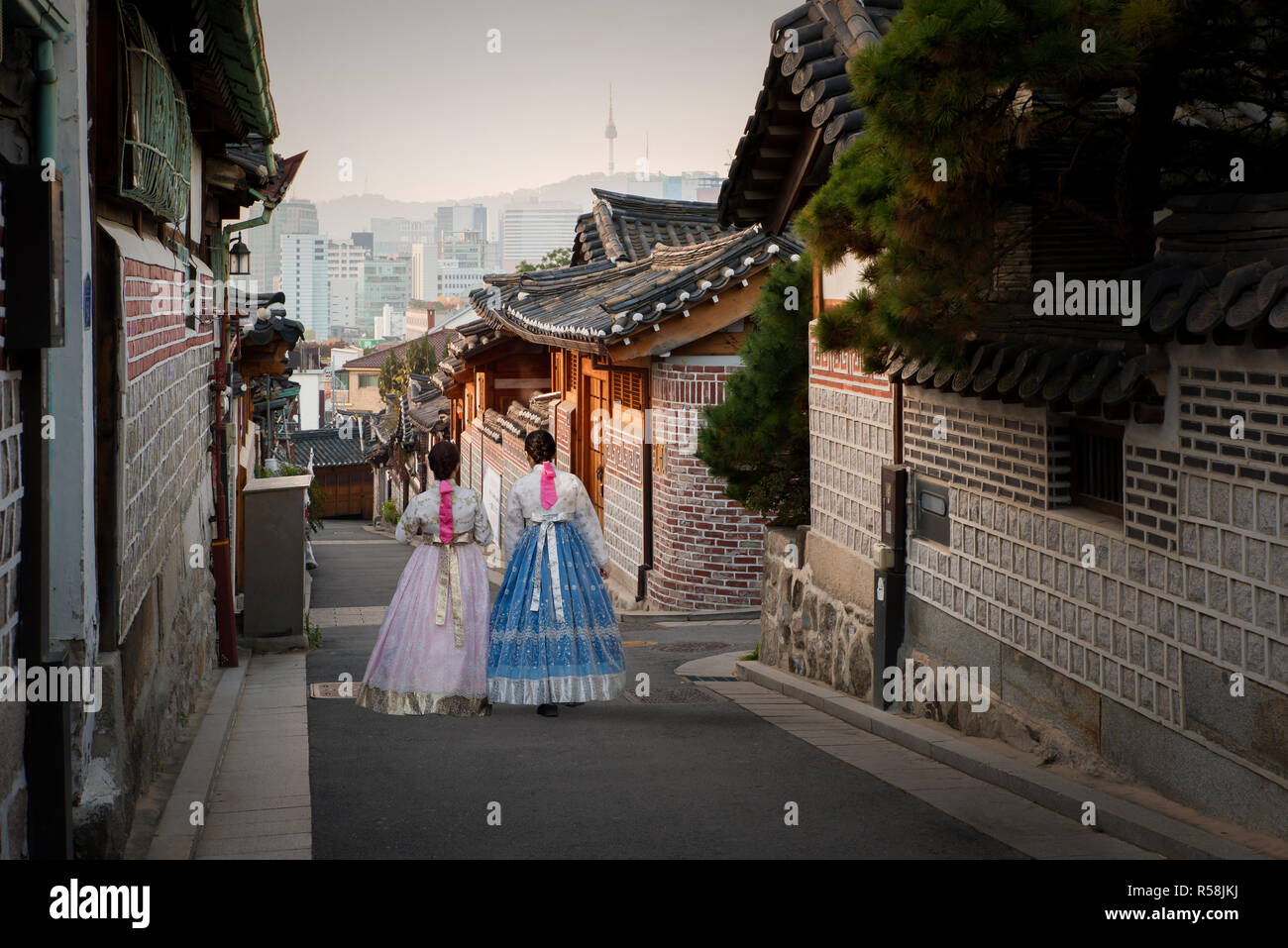 Back of two women wearing hanbok walking through the traditional style houses of Bukchon Hanok Village in Seoul, South Korea. Stock Photo