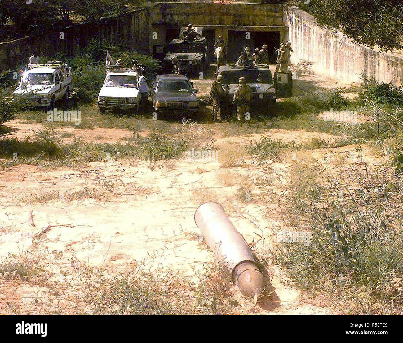 The entrance of one an estimated 38 bunkers discovered, just north of Mogadishu, Somalia, by MPs from the 511th Military Police Company, Fort Drum, New York. The MPs escort members of the media into the bunker. Two M998 High-Mobility Multipurpose Wheeled Vehicles (HMMWV) are parked near the entrance along with three vehicles driven by the media. A large unidentifiable artillery shell is seen in the foreground. This mission is in direct support of Operation Restore Hope. Stock Photo