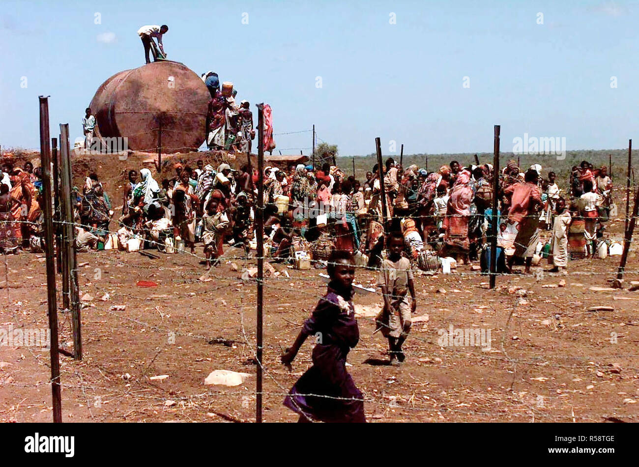 A Group of Somali refugees gathers behind barbed wire fence to get water from a well. The well was drilled by the Indian Army to provide the refugees on Baidoa, Somalia with fresh water. This mission is in direct support of Operation Restore Hope. Stock Photo
