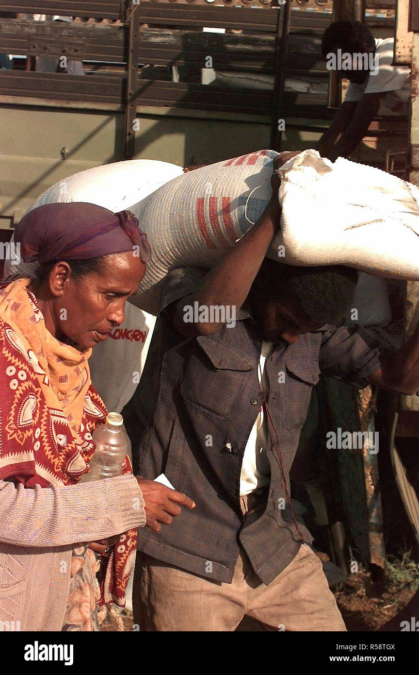 1993 - Straight on shot of a Somali man carrying a 50 Kilogram bag of maize over his head.  He carries it for a Somali woman that is left in the frame.  The food is being distributed by the Irish relief organization Concern.  The food and supplies provided are in direct support of Operation Restore Hope. Stock Photo