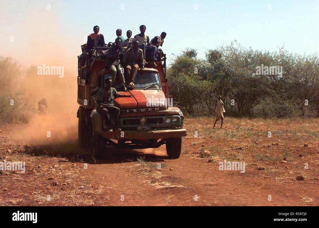 1993 - Straight on shot of a late model Isuzu dump truck loaded with Somali men.  One man rides on the right front fender while two others ride on the top of the truck's cab.  They are from the village of Maleel and are arriving at the landing zone where bags of wheat are being delivered (not shown).  This mission is in direct support of Operation Restore Hope. Stock Photo