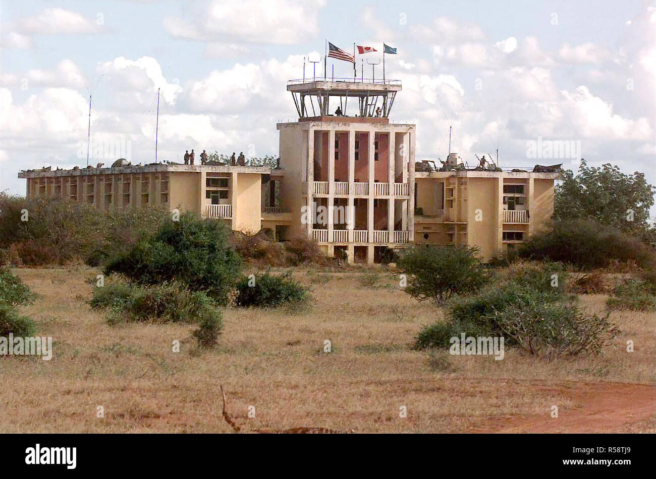 1992 - Soldiers from combined US and Canadian Forces secure an abandoned headquarters and control tower building at Baledogle, Somalia.  Members of the 10th Mountain Division, Fort Drum, New York and Air Force Combat Controllers are seen on the roof and in the control tower.  The flags of the United States, Canada and United Nations fly over the control tower.  This mission is in support of Operation Restore Hope. Stock Photo