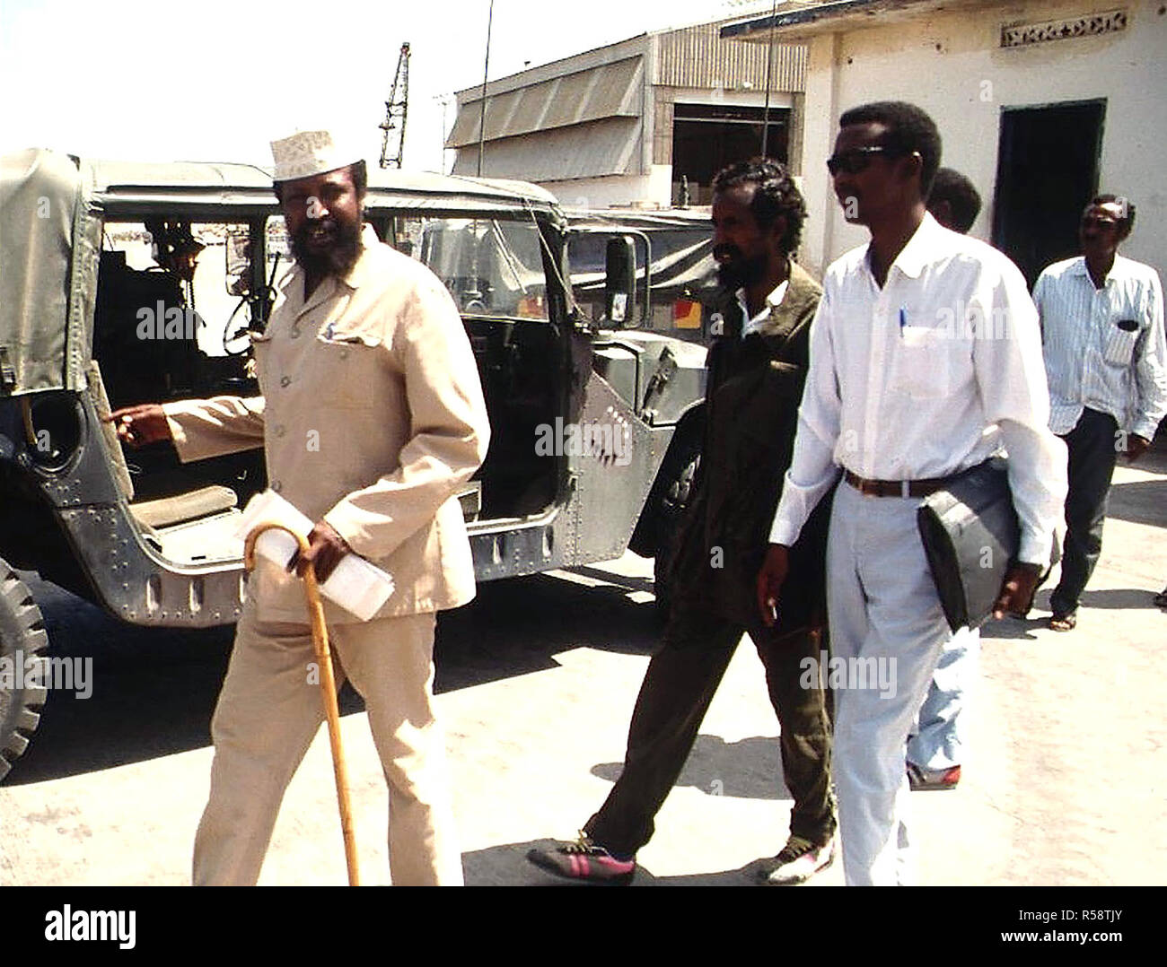 1992 - Straight on shot of Somali Faction Leader COL Jess, at left with hat and cane, walking outside the Joint Task Force Headquarters in Kismayo, Somalia with his entourage.  He had just completed a meeting with BGEN Lawson Magruder, USA, Joint Task Force Commander in Kismayo.  BGEN Magruder, (not shown) is from the 10th Mountain Division Fort Drum, New York.  This mission is in direct support of Operation Restore Hope. Stock Photo