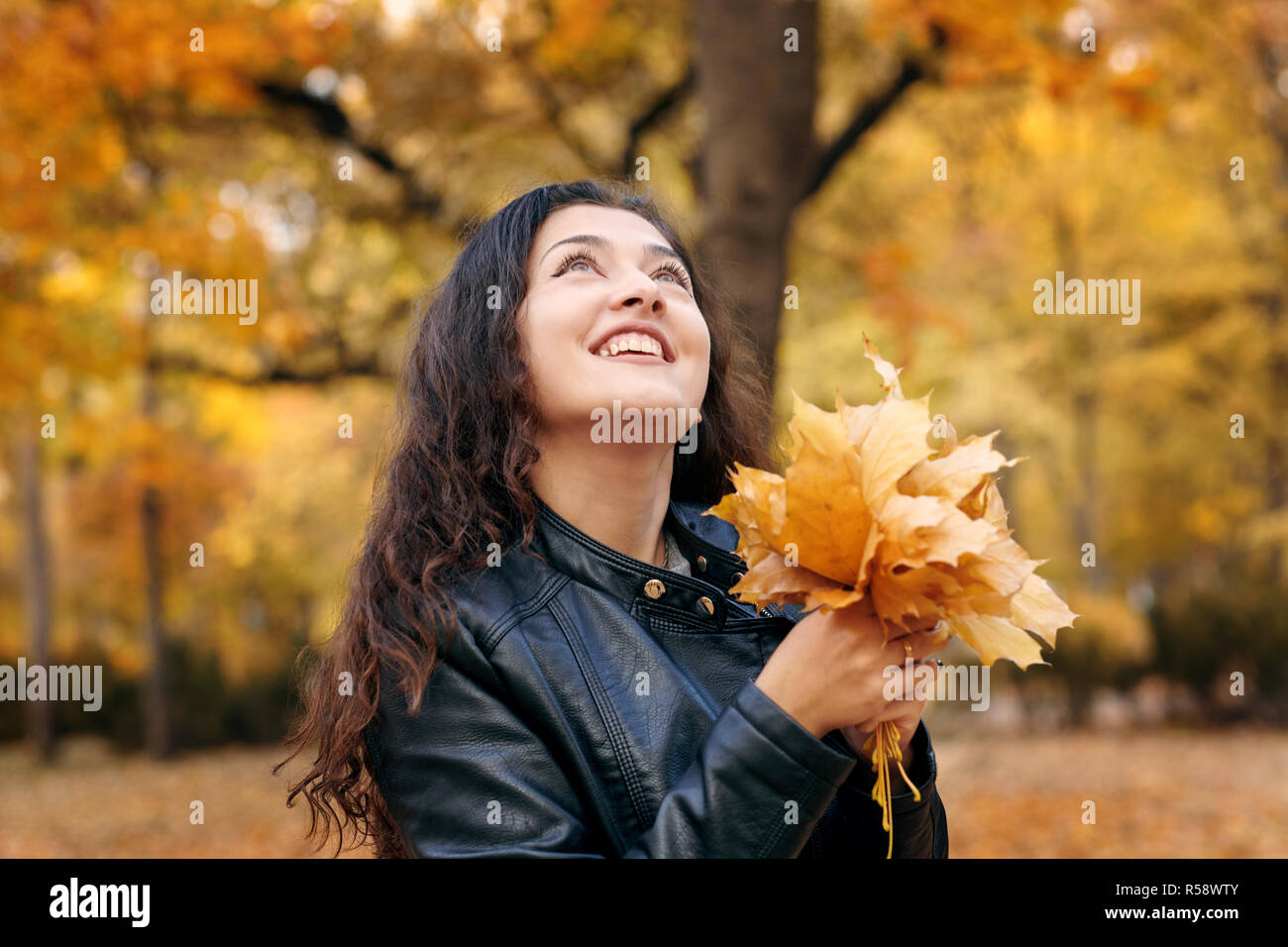 Pretty woman is posing with bunch of maple's leaves in autumn park ...