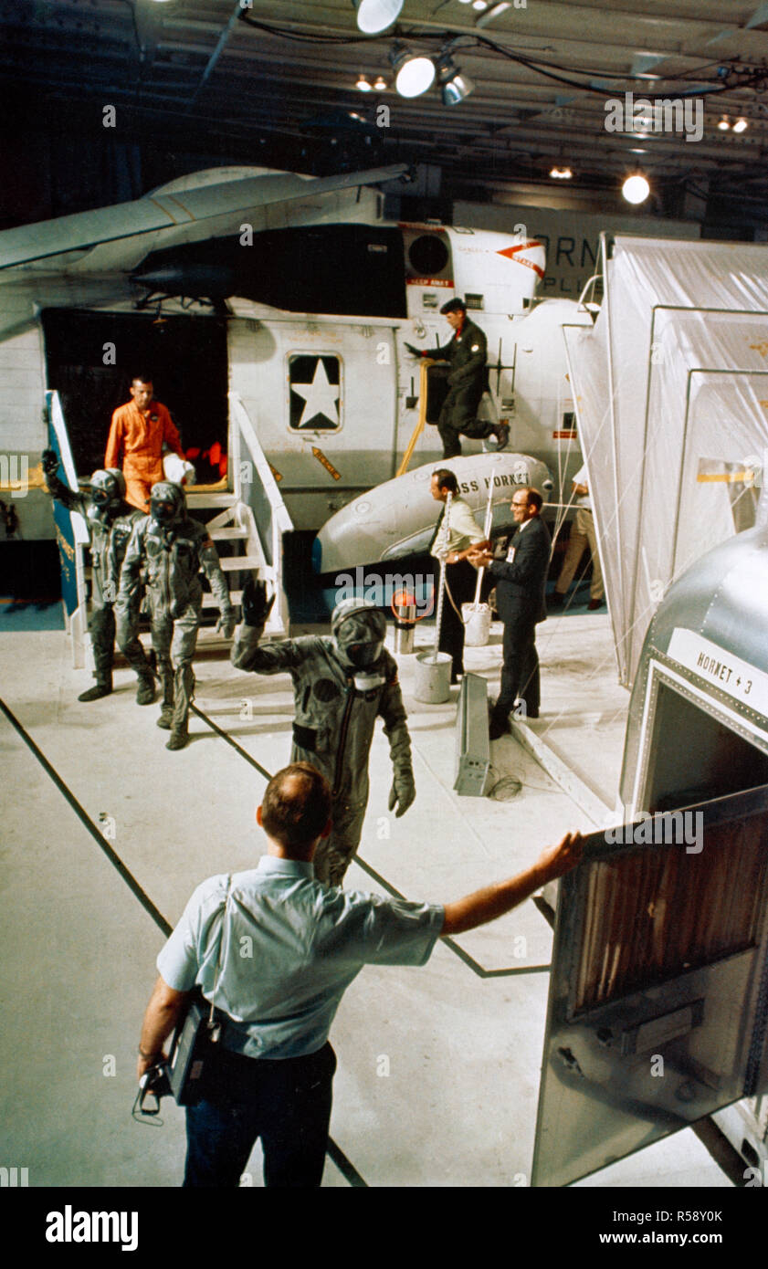 (24 July 1969) --- The Apollo 11 crewmen, wearing biological isolation garments, arrive aboard the USS Hornet during recovery operations in the central Pacific. They are walking toward the Mobile Quarantine Facility (MQF), in which they will be confined until they arrive at the Manned Spacecraft Center's (MSC), Lunar Receiving Laboratory (LRL). Stock Photo