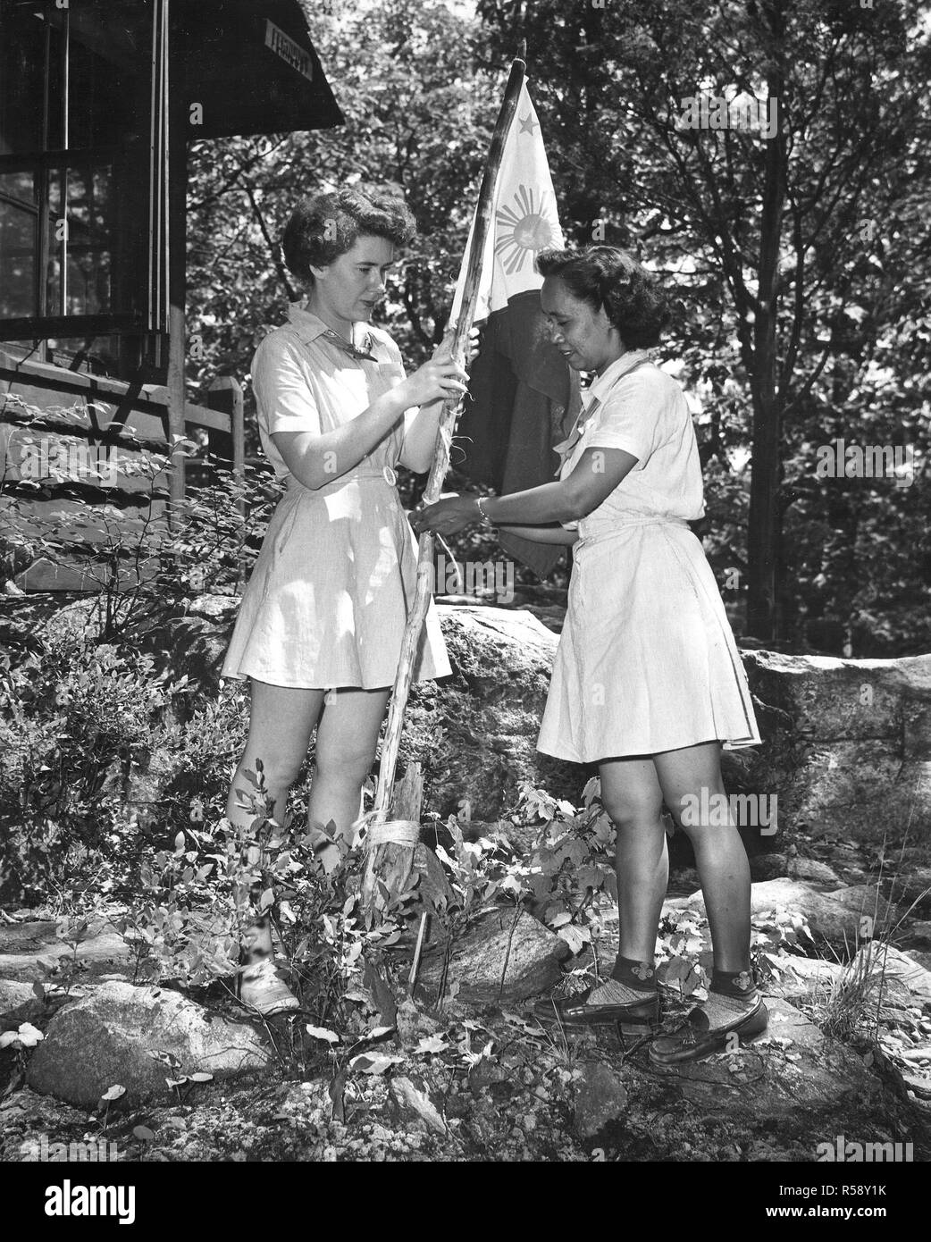 Photograph of Miss Ross D. Valencia, Assisted by Ruth Cuniff, Raising Her  Nation's Flag of the Republic of the Philippines Outside Her Cabin at Edith  Macy Training School in Pleasantville, New York