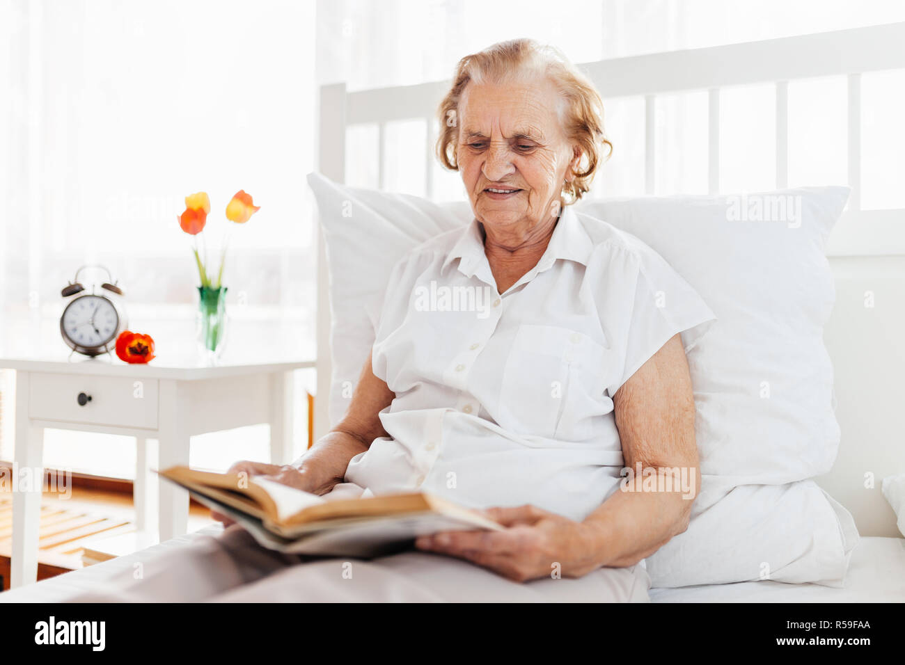 Elderly woman sitting comfortably in bed reading her favourite book