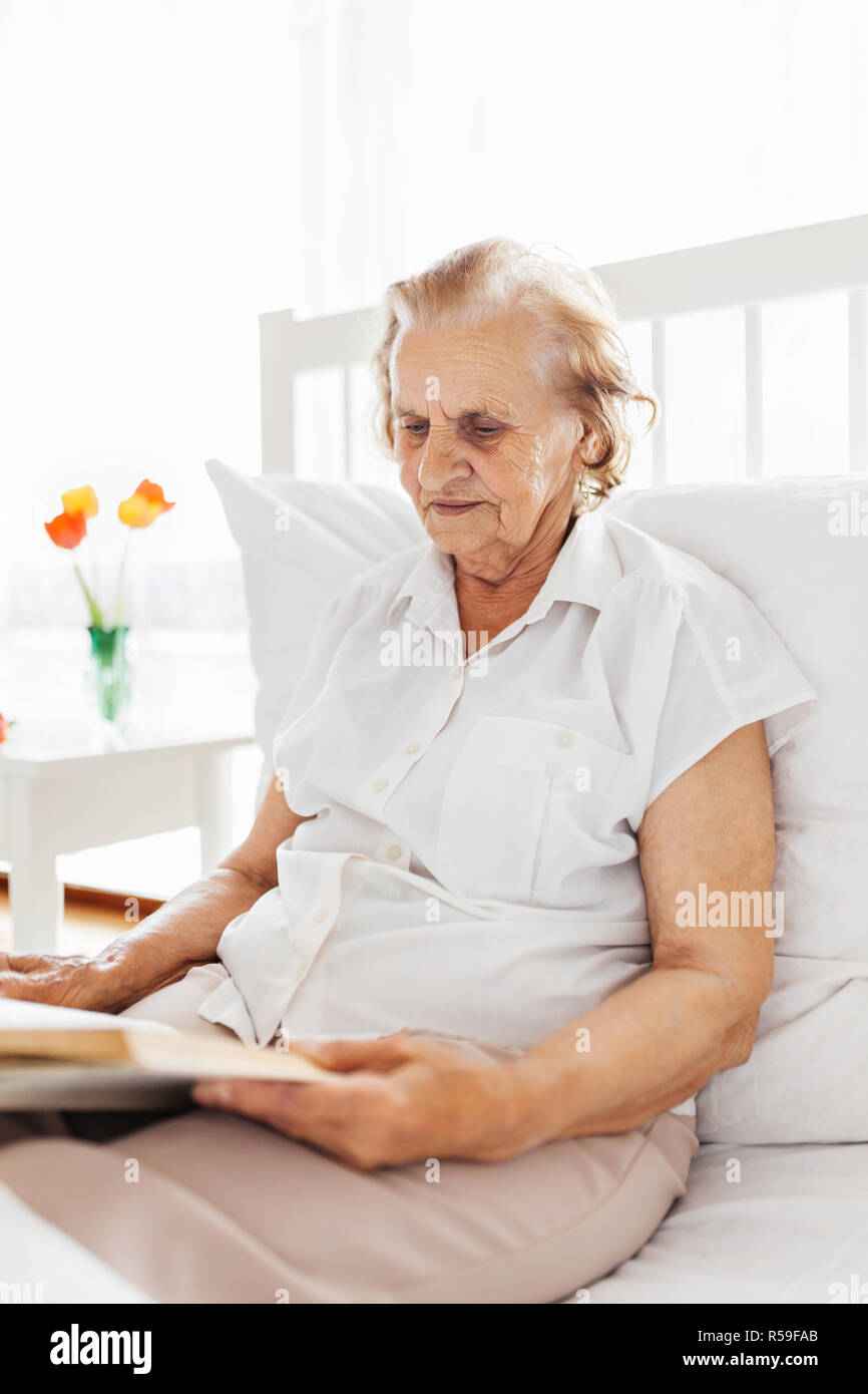 Elderly woman sitting comfortably in bed reading her favourite book