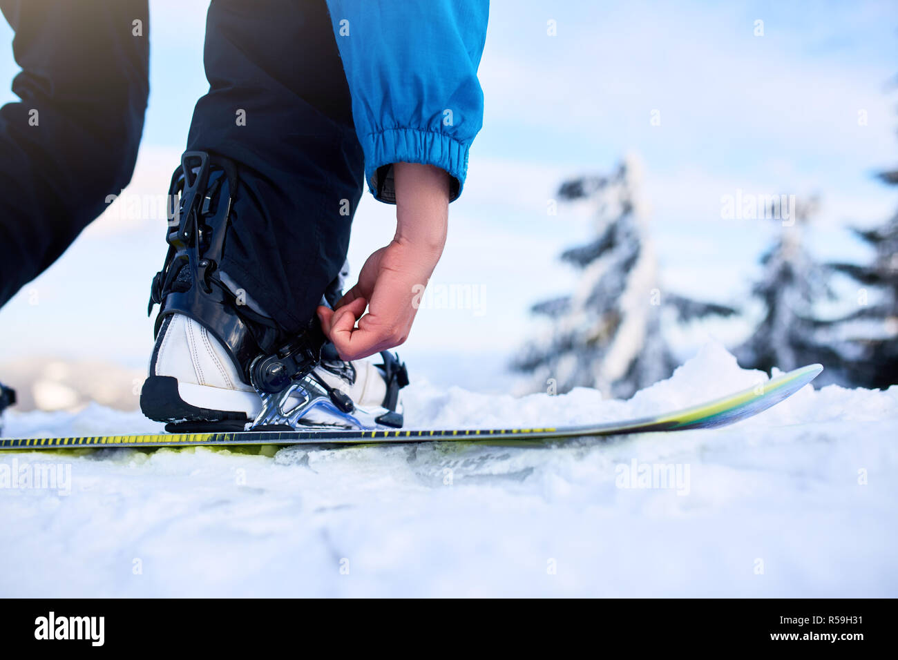 Snowboarder straps in his legs in snowboard boots in modern fast flow bindings with straps. Rider at ski resort prepares for freeride session. Man wearing fashionable outfit. Stock Photo