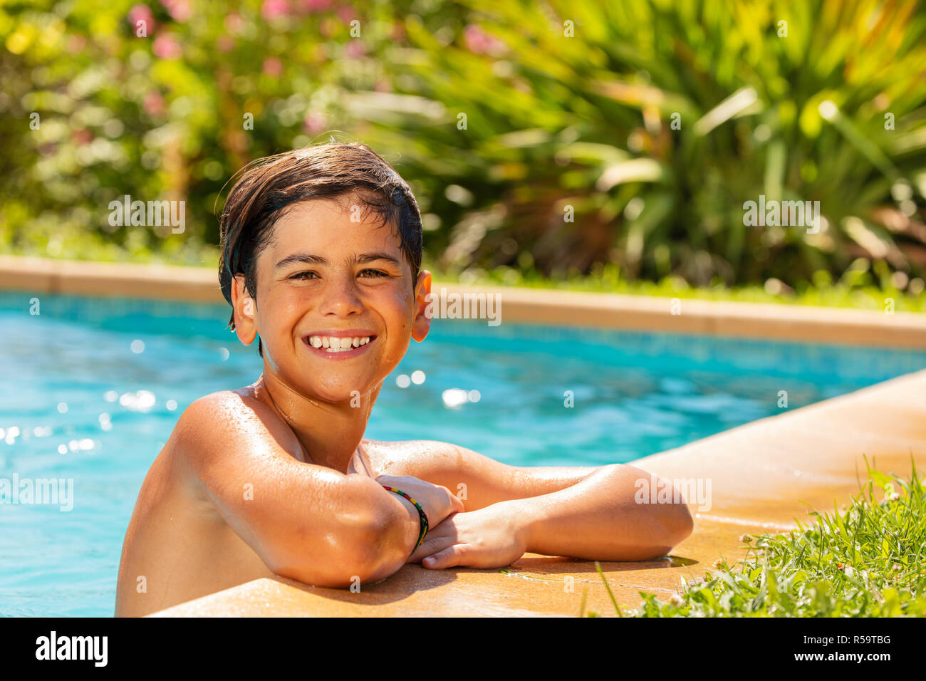 Portrait of smiling teenage boy relaxing at outdoor swimming pool in