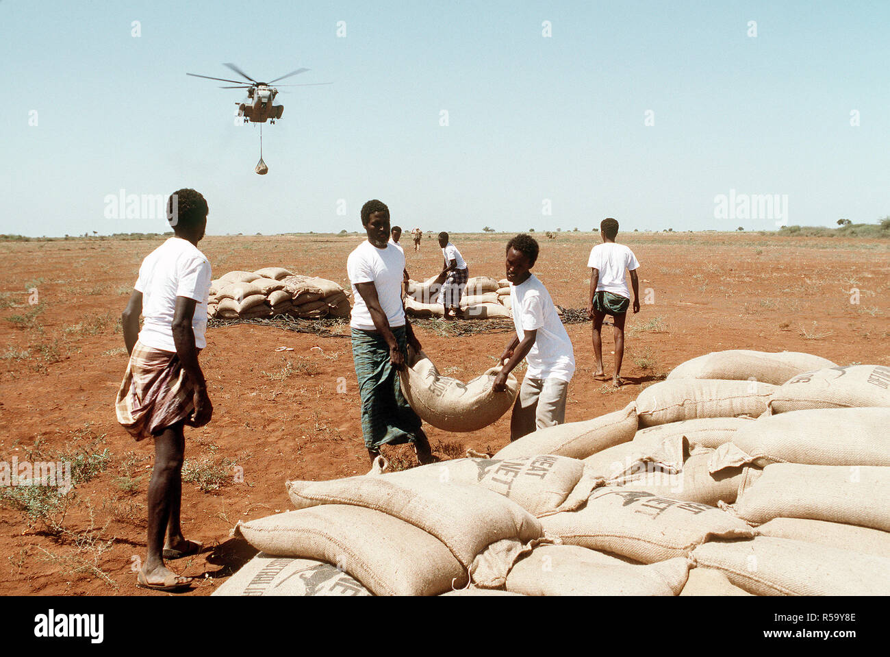 1993 - Men from the village of Maleel stack bags of wheat as a Marine Heavy Helicopter Squadron 363 (HMH-363) CH-53D Sea Stallion helicopter prepaers to drop another load during the multinational relief effort OPERATION RESTORE HOPE. Stock Photo