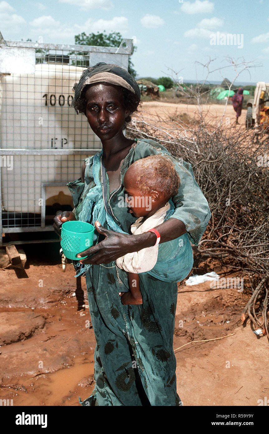 1993 - A Somali refugee woman holds her child as they stand near a water dispenser at an aid station set up during Operation Restore Hope relief efforts (Badera Somalia) Stock Photo