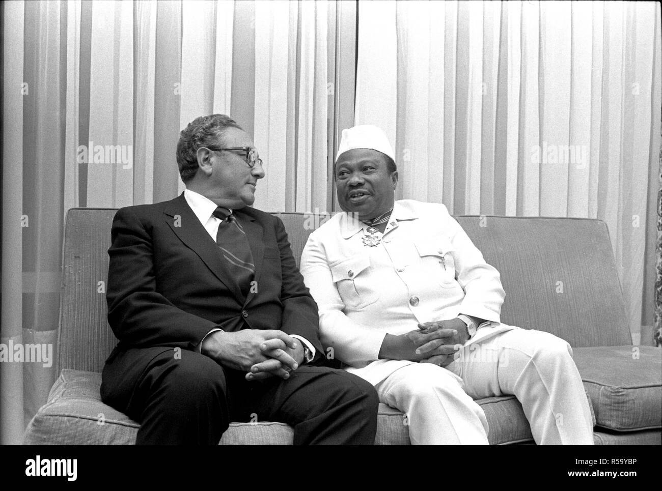 1976, April 30 – Executive Mansion – Monrovia, Liberia (Africa) – Henry Kissinger, William T. Tolbert Jr. – seated together on sofa, talking, laughing – Secretary of State Trip to Africa; Stock Photo
