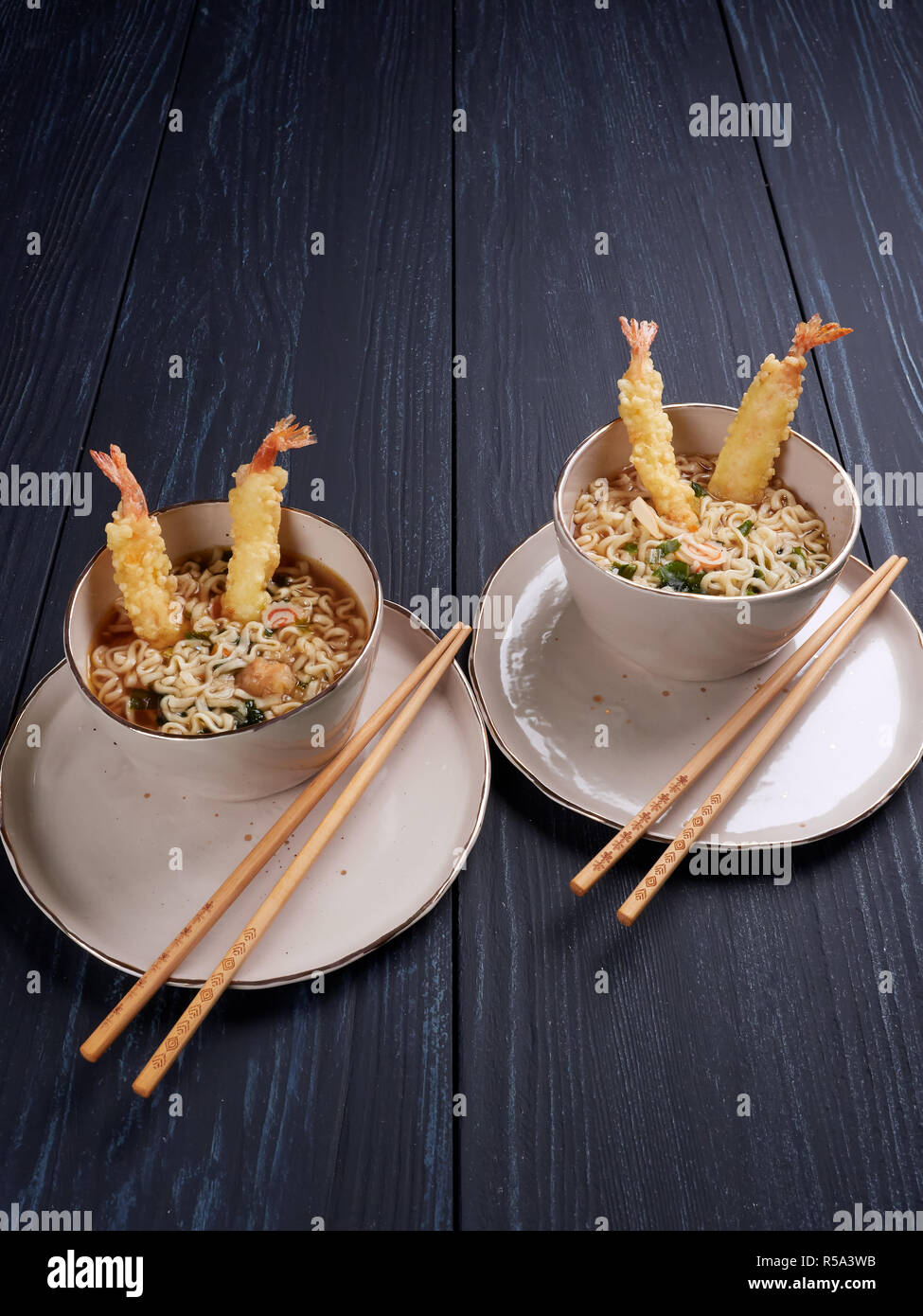 Two bowls of tempura udong noodles, with shrimps temputa, in beige bowls with wooden chopsticks, on dark blue background Stock Photo