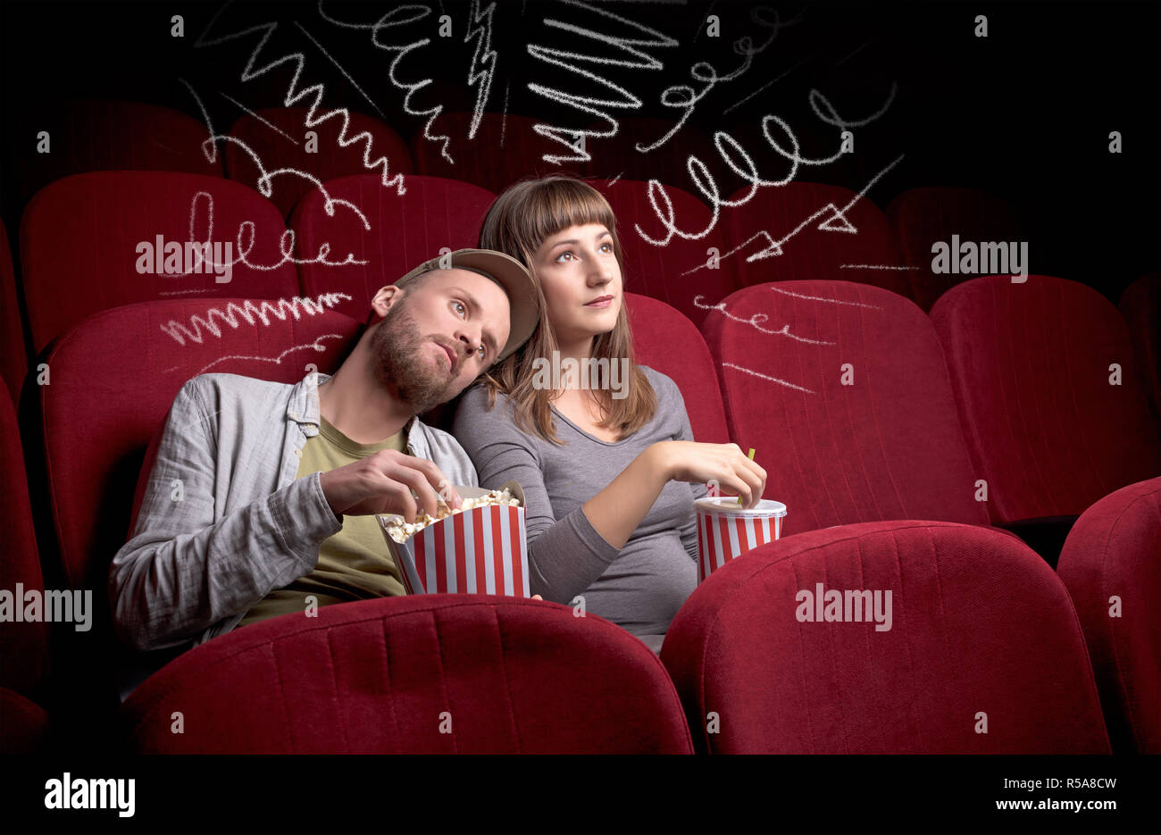 Young cute couple sitting in cinema, and eating popcorn while watching