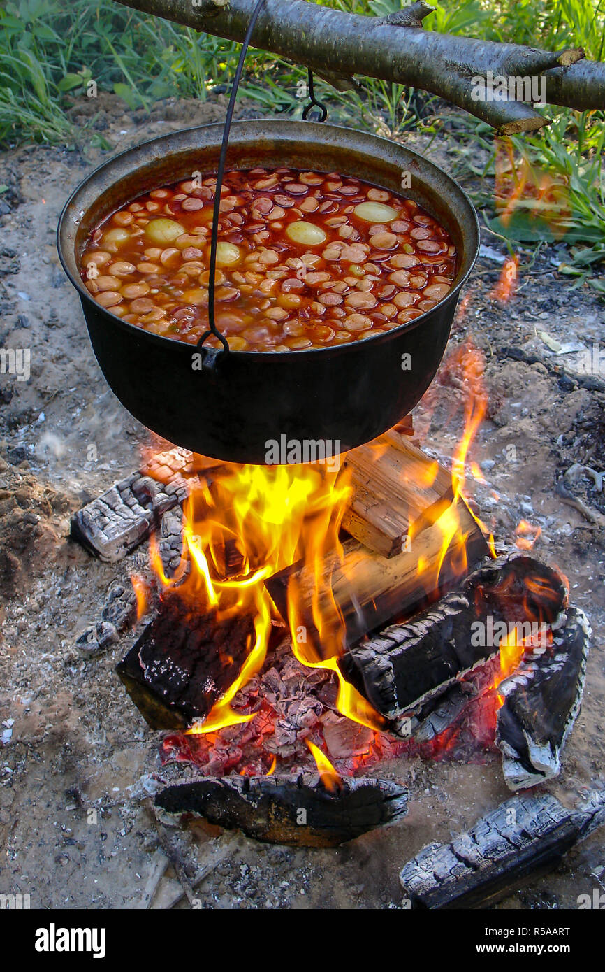Cooking soup in cast iron boiler on burning campfire. Pot with soup