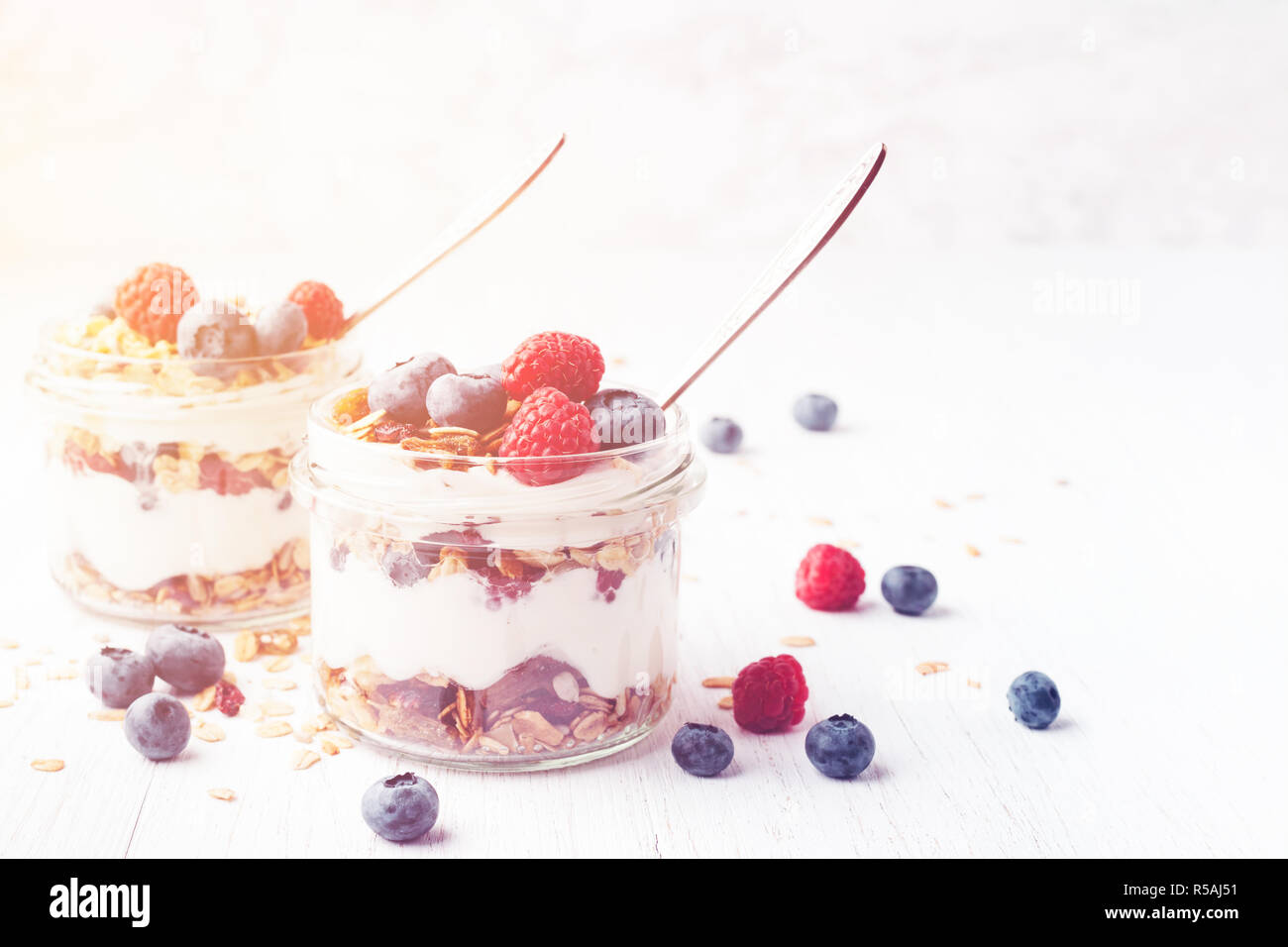 Two jars with tasty parfait made of granola, berries and yogurt on white wooden table. Shot at angle. Toned image with copy space. Stock Photo