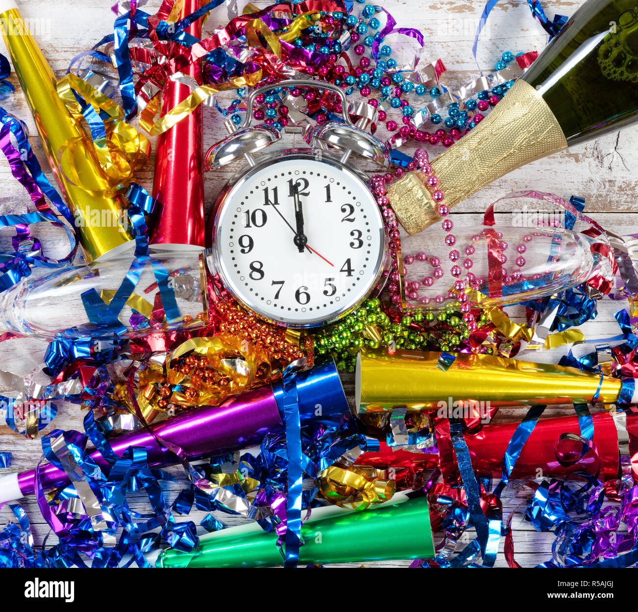 Happy New Year Celebration with clock striking twelve in center of party objects on white rustic wood Stock Photo