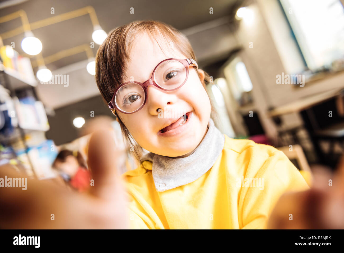 Yellow sweater. Close up of pleasant cute girl with Down syndrome wearing bright yellow sweater Stock Photo