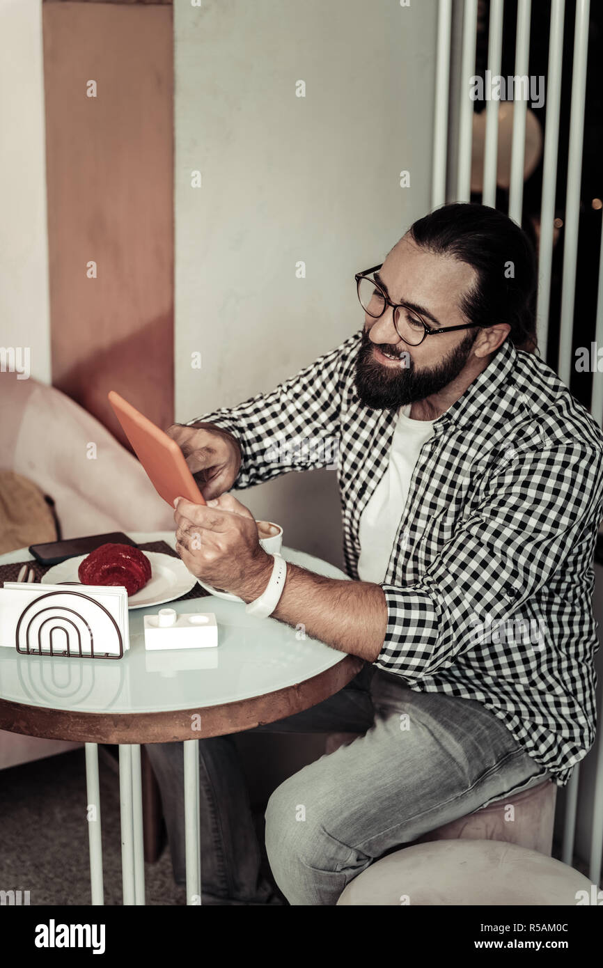Modern gadget. Cheerful bearded man using his tablet while checking his social networks Stock Photo