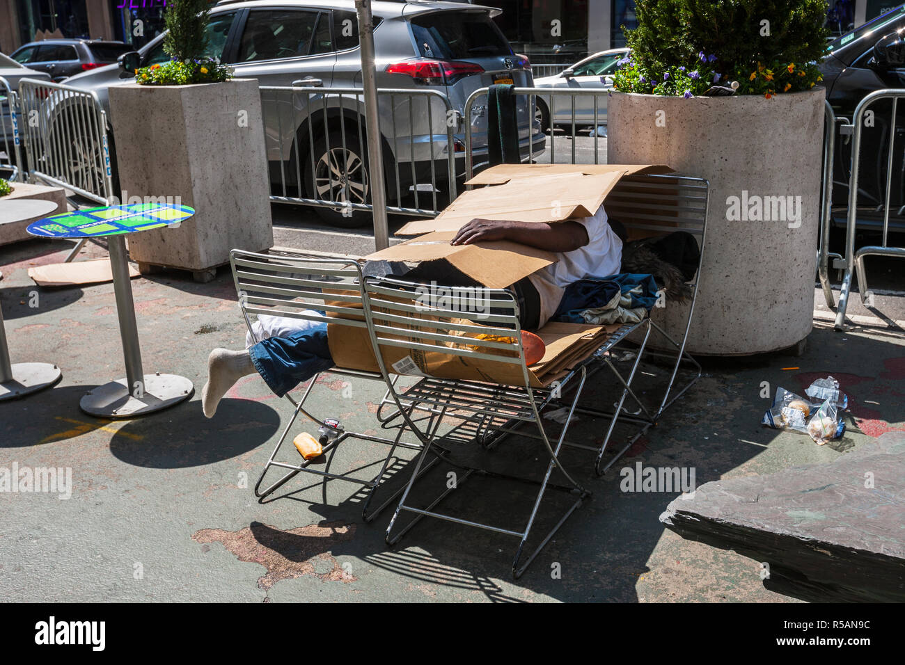 Homeless man covered with cardboard sleeping on the street in Manhatan New York Stock Photo