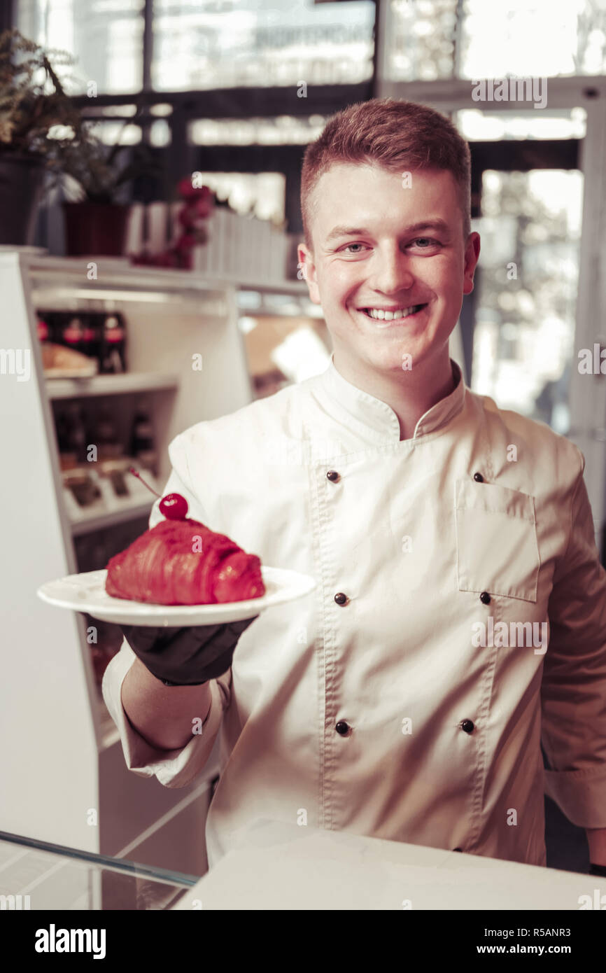 My masterpiece. Cheerful happy pastry chef smiling to you while holding