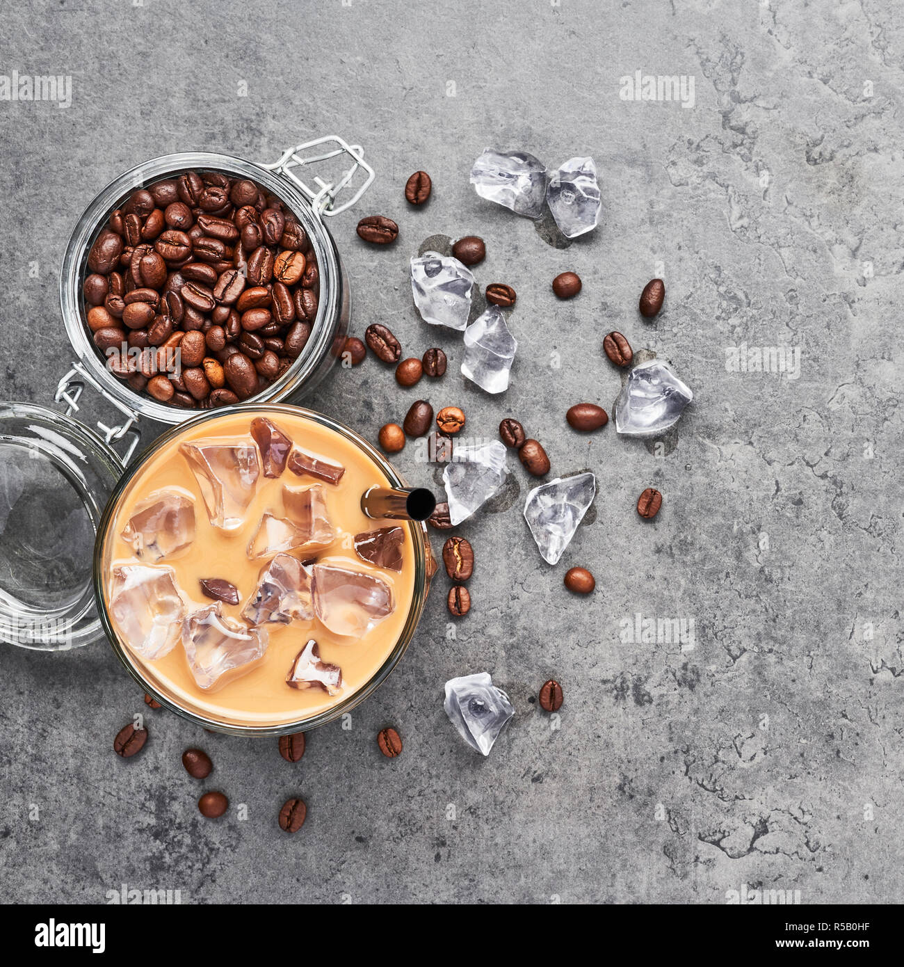 Cold brewed iced coffee in glass and coffee beans in glass jar on grey concrete background. Chocolate, vanilla, caramel or cinnamon iced coffee in tal Stock Photo