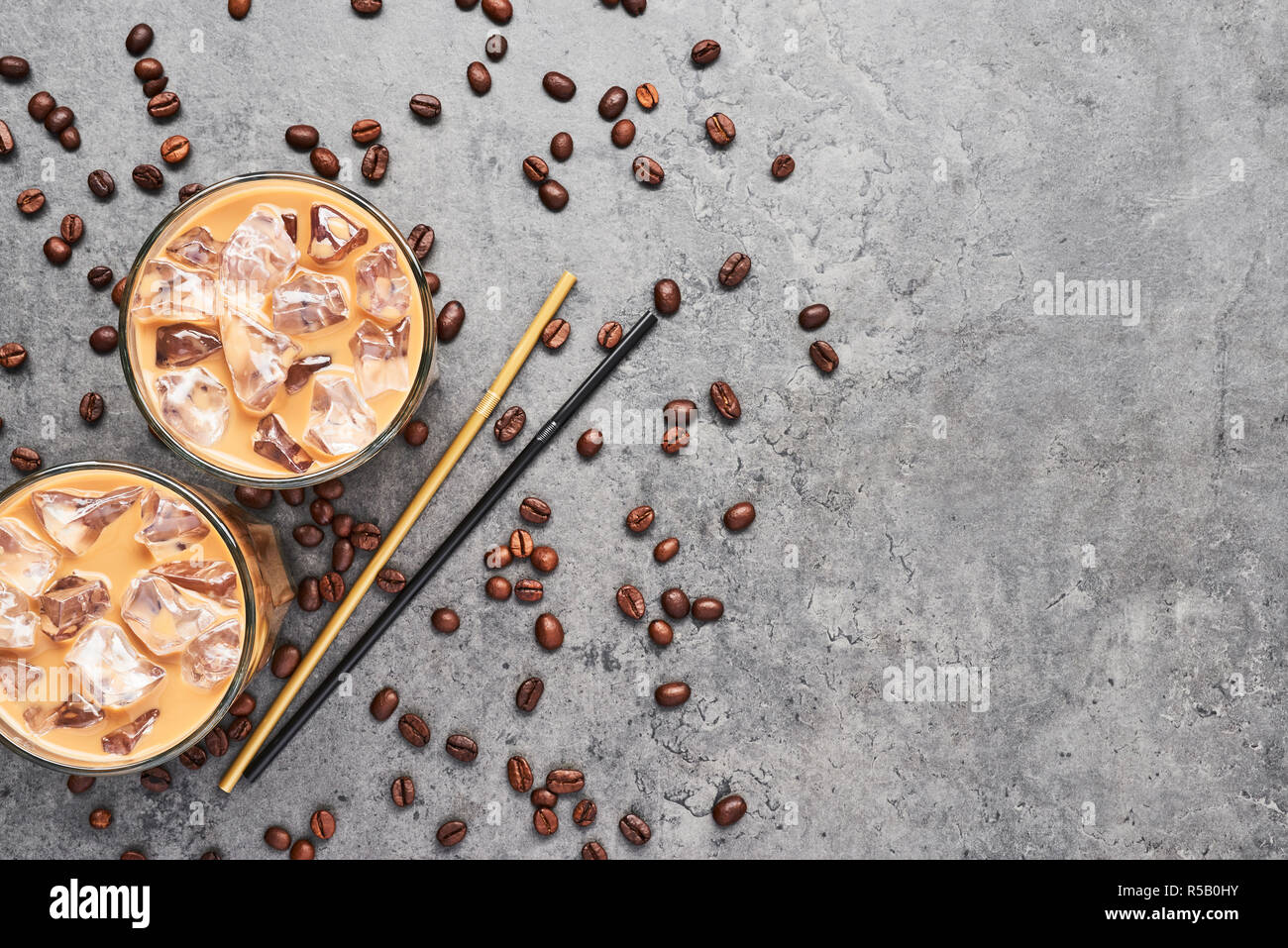 Cold brewed iced coffee in tall glass with coffee beans and straws on grey concrete background. Chocolate, vanilla, caramel or cinnamon iced coffee in Stock Photo