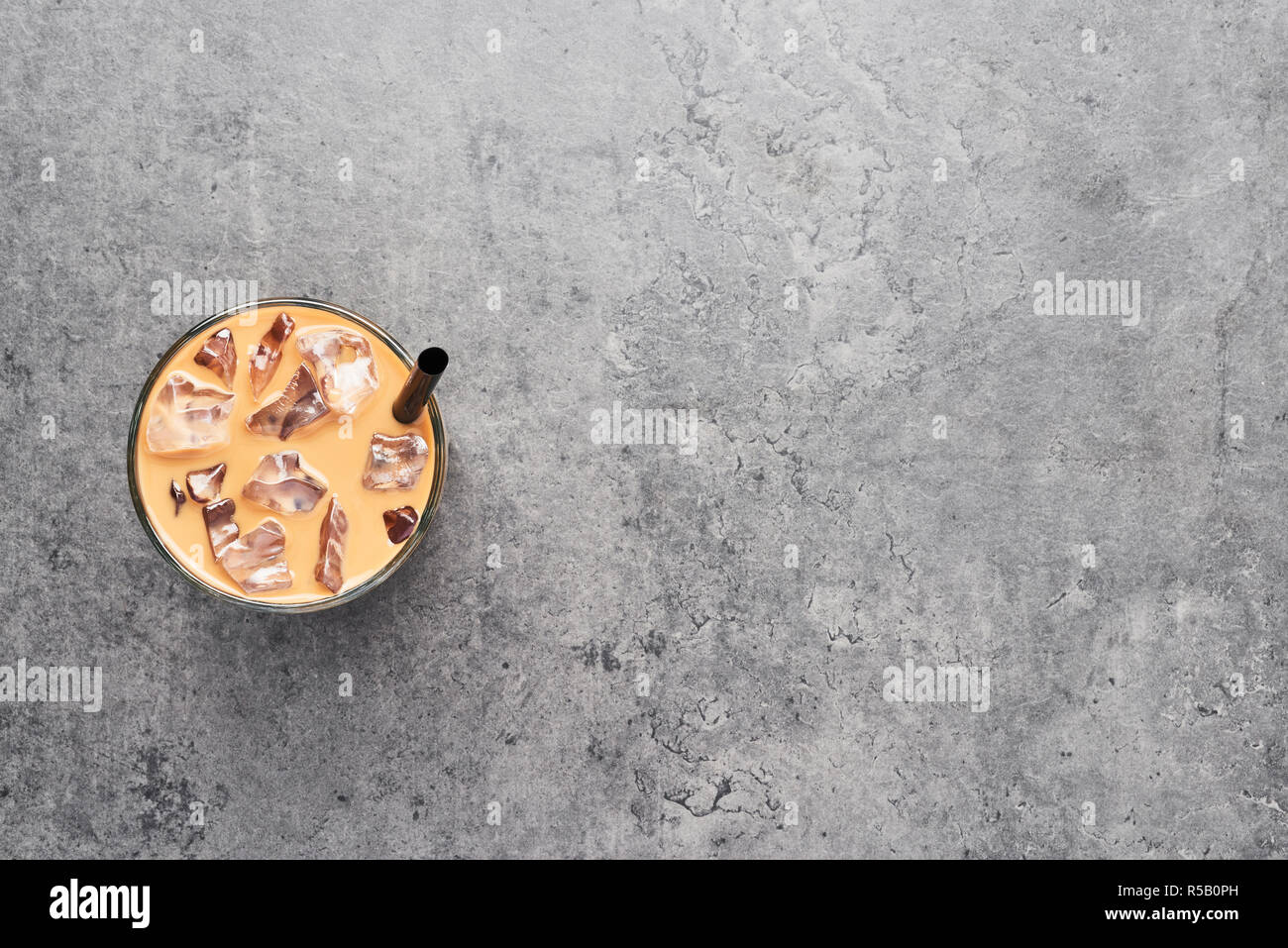Chocolate, vanilla, caramel or cinnamon iced coffee in tall glass with black straw on grey concrete background. Top view with copy space for text. Stock Photo
