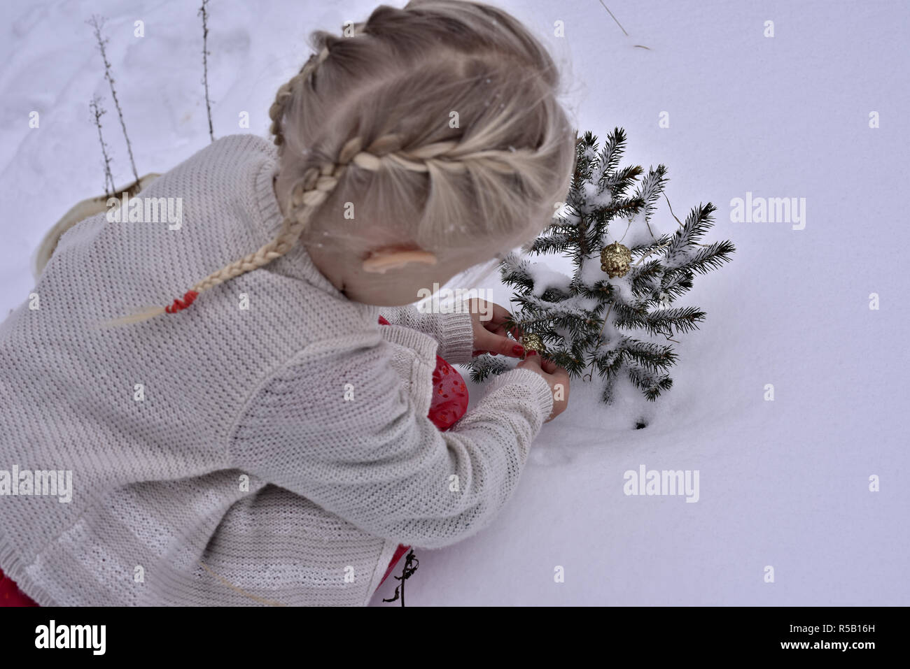 Beautiful little girl finds the spirit of Christmas by decorating an outdoor pine tree fluffed in snow Stock Photo