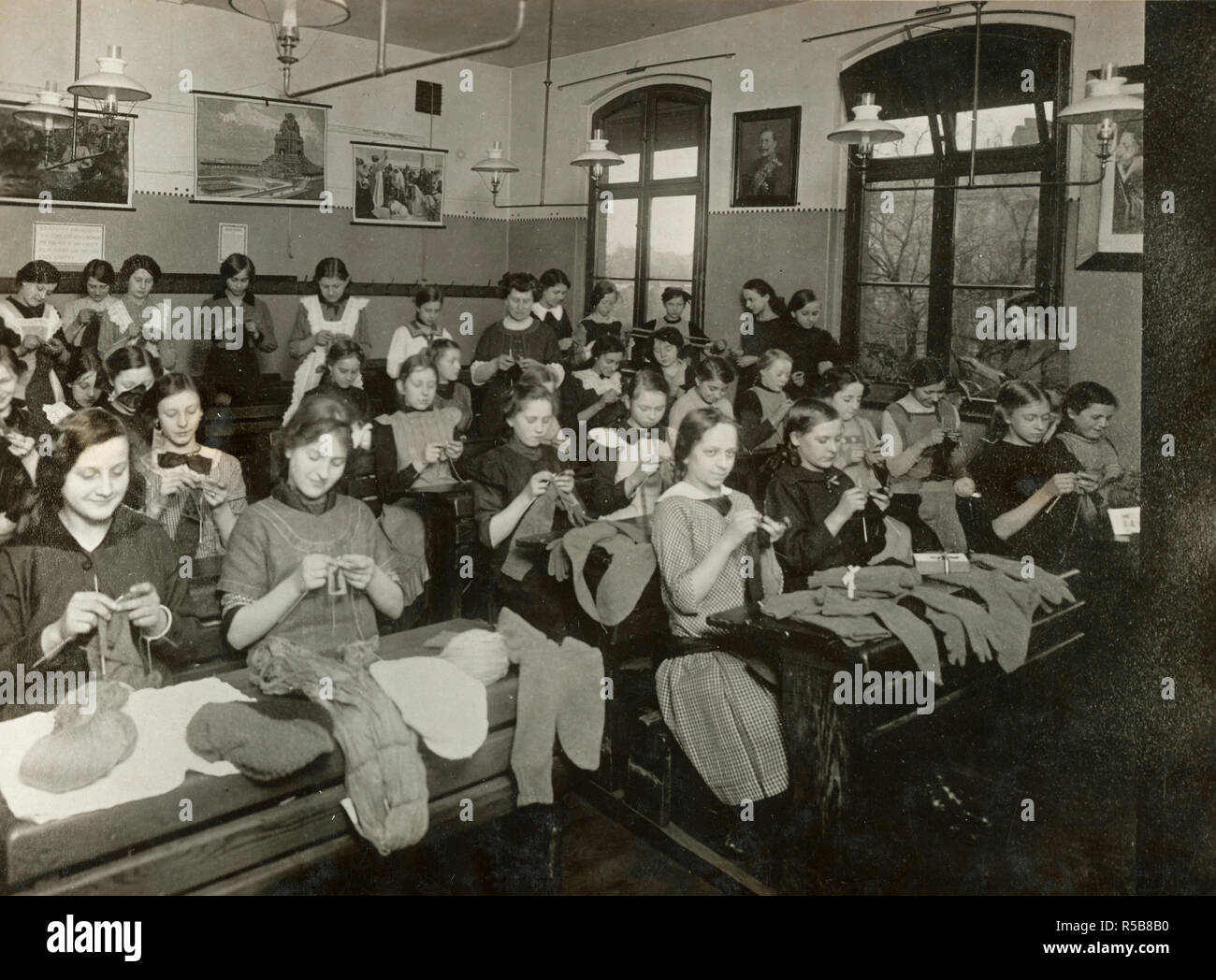 School children in domestic science classes learning to knit socks for the soldiers in the field. Good propaganda picture. Note Kaiser between biblical subjects on the wall ca. 1918 Stock Photo