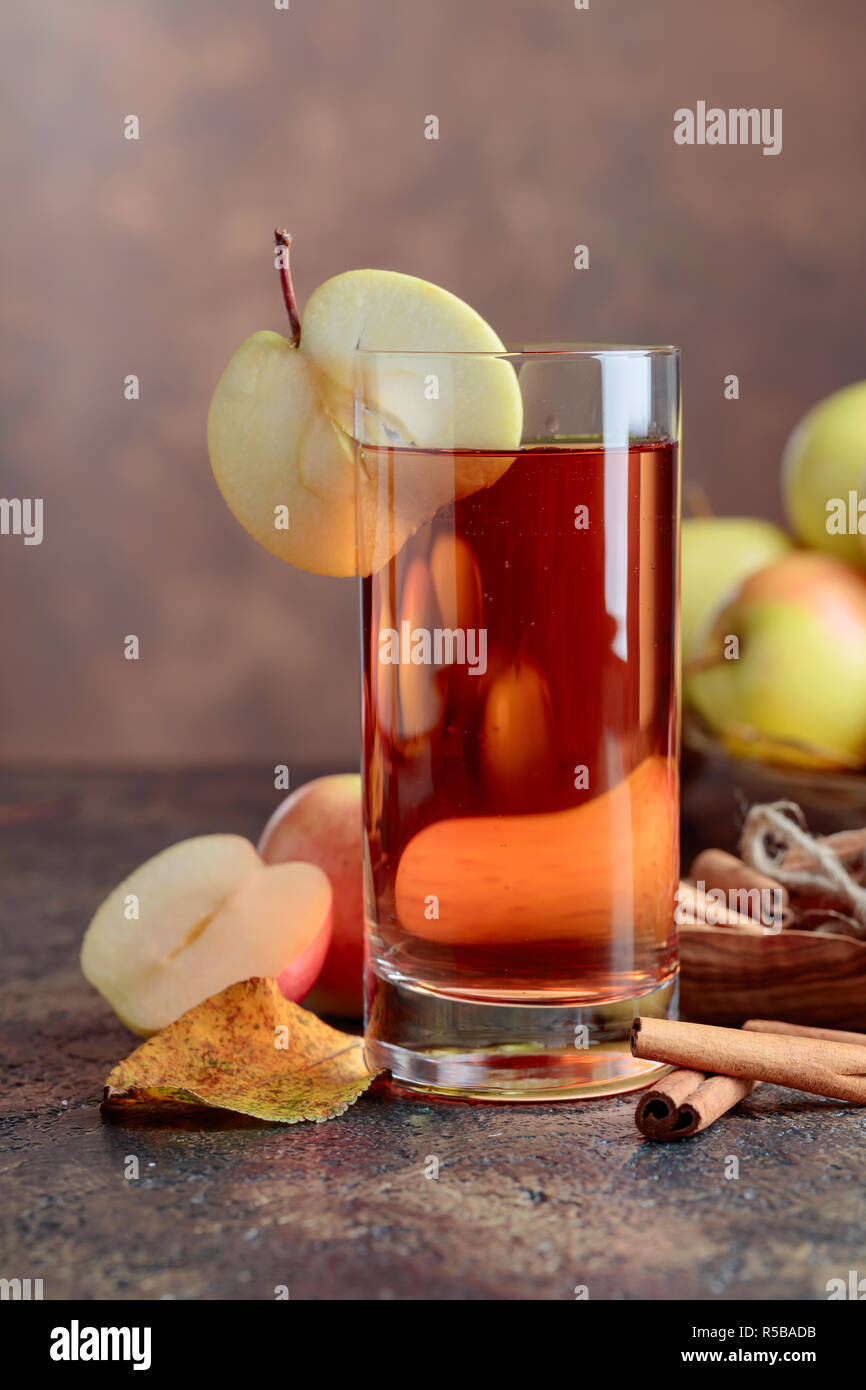 Glass of apple juice or cider with juicy apples and cinnamon sticks on a kitchen table. Stock Photo