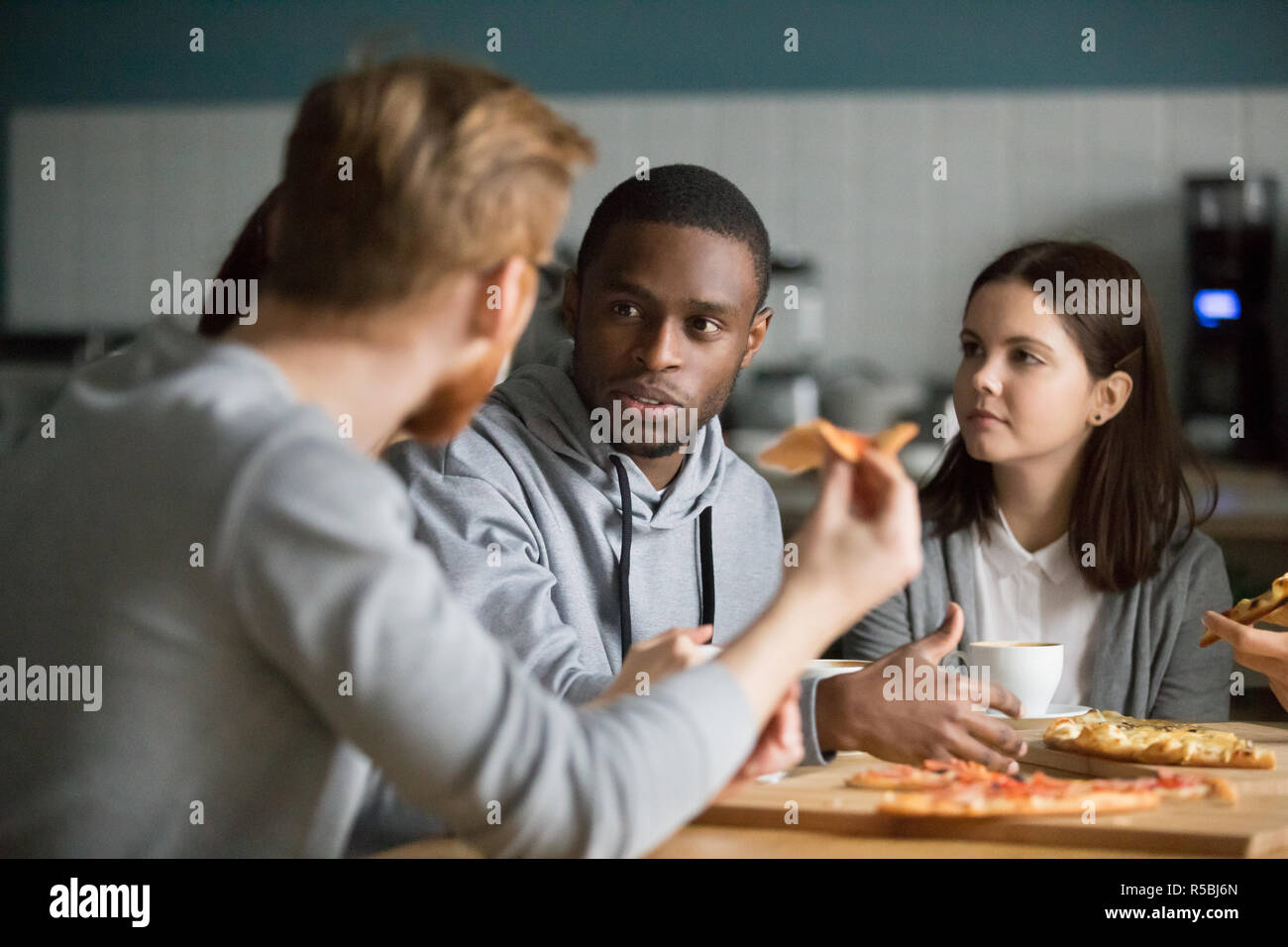 Multiethnic millennial colleagues talk meeting in pizzeria for lunch, diverse friends have conversation hanging out together in cafe, young people spe Stock Photo