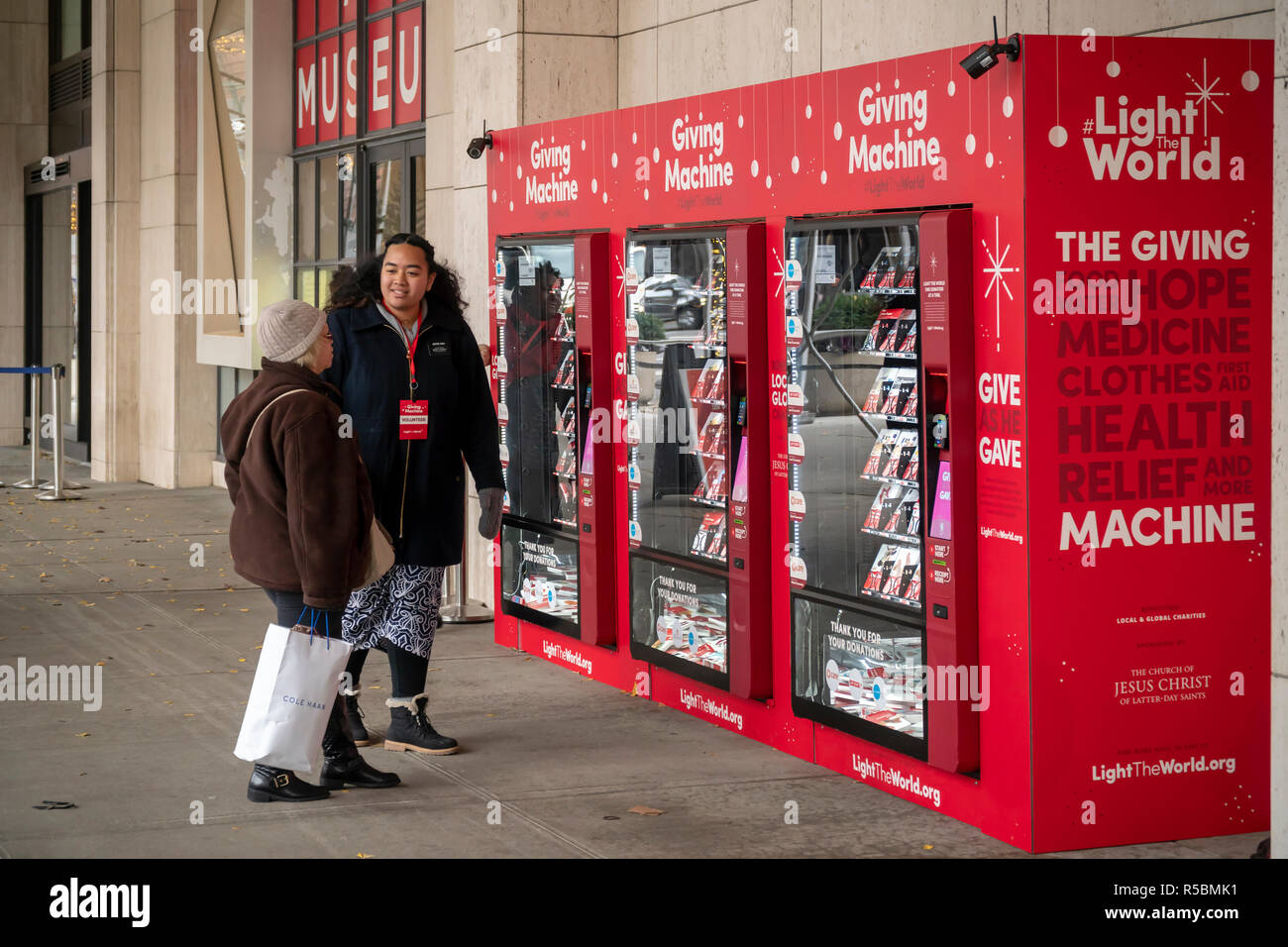 Just in time for #givingtuesday, volunteers explain the “Giving Machines' outside the LDS Church in New York on Giving Tuesday, November 27, 2018. The vending machines created by The Church of Jesus Christ of Latter-day Saints enable participants to purchase items, from socks to a goat, that will be distributed to aid organizations. The LDS covers the machines and any associated administrative costs so 100% of the donations goes to the partner charities both local and international. The machines will be around until the end of December. (© Richard B. Levine) Stock Photo