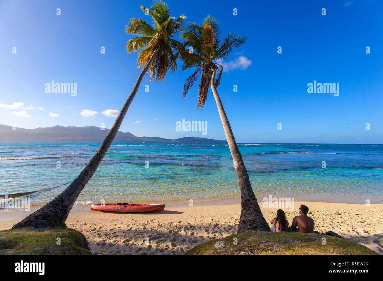 Dominican Republic, Samana Peninsula, Las Galleras, La Playita beach, Couple sitting by palm tree Stock Photo