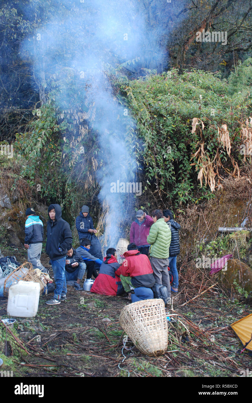 porters warm themselves around a fire next to a small shack in the forests of Eastern Nepal Stock Photo