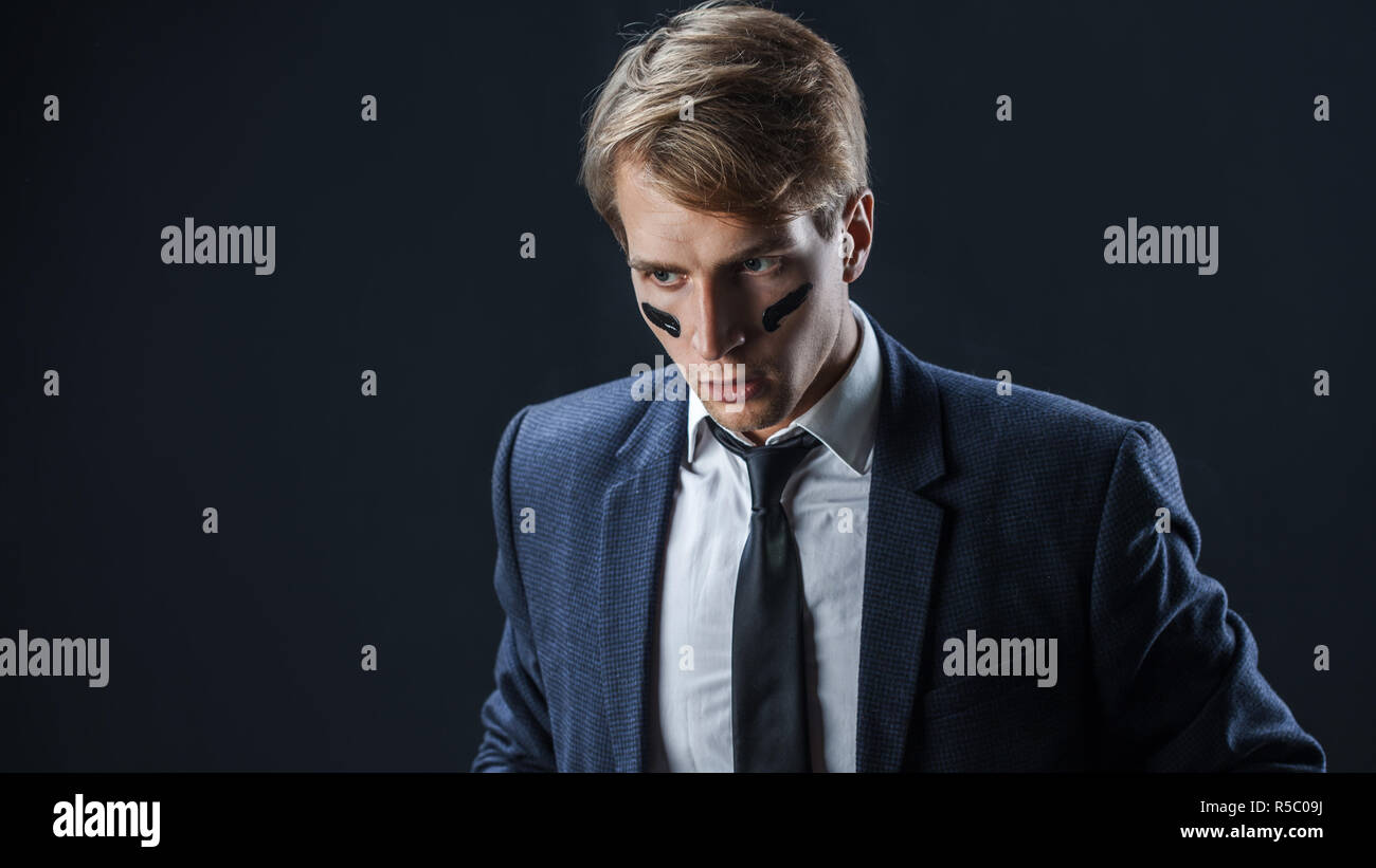 Serious and thoughtful young man in a business suit with war paint on his face. Aggressive business, concept Stock Photo