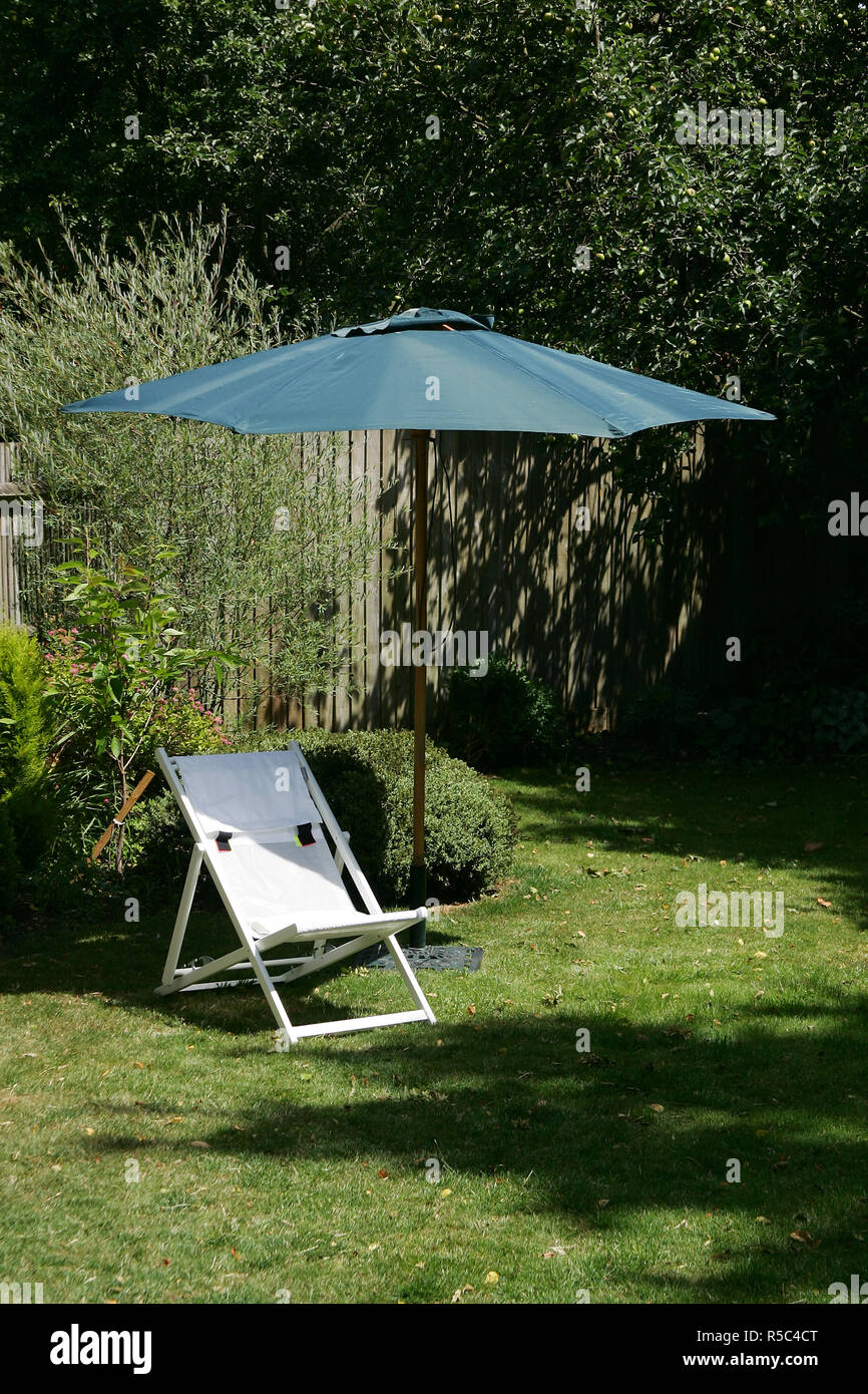 A deck chair and sunshade / parasol in a garden on a summer day Stock Photo