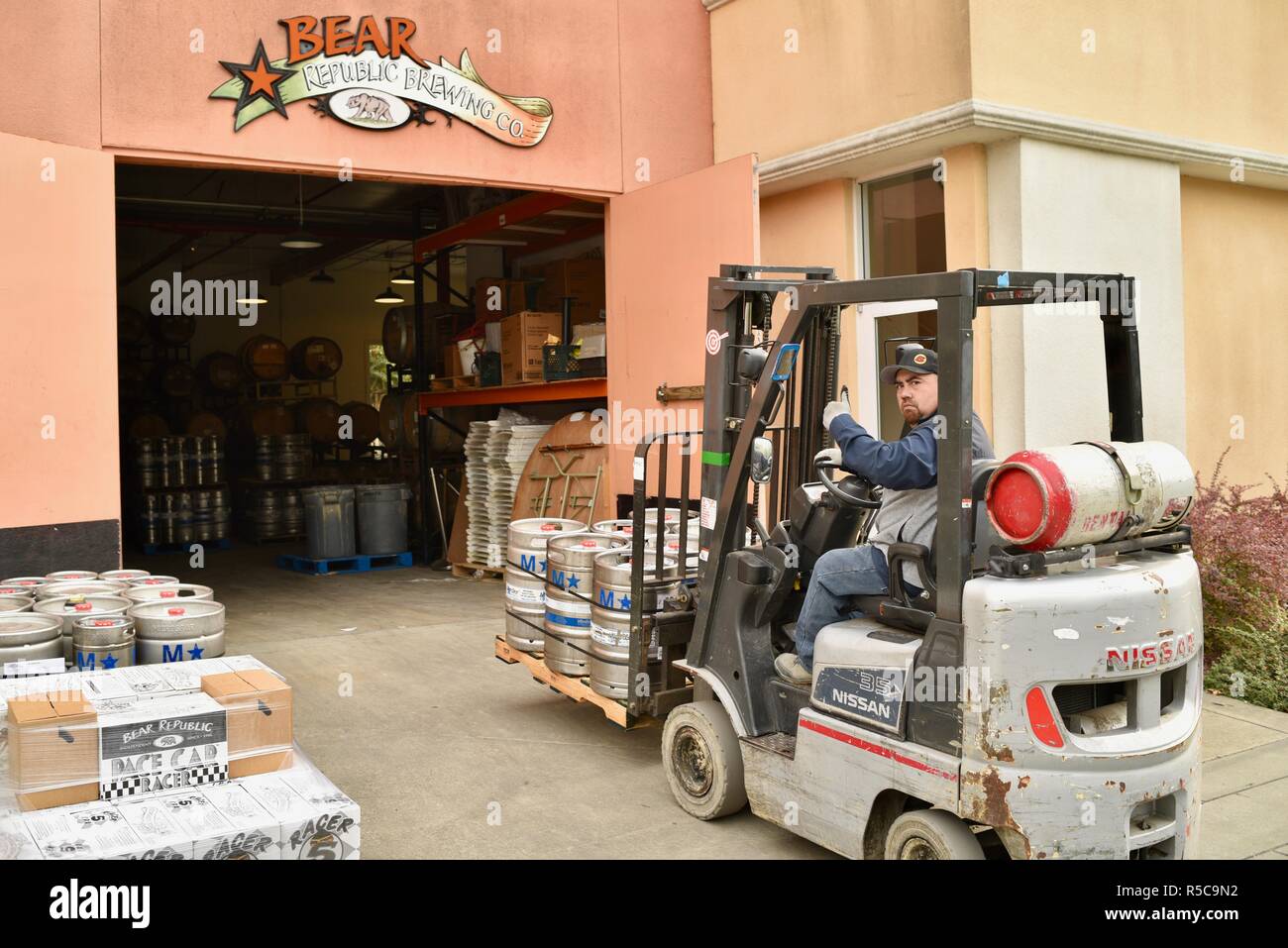 Brewery warehouse male worker driving forklift moving barrels of beer