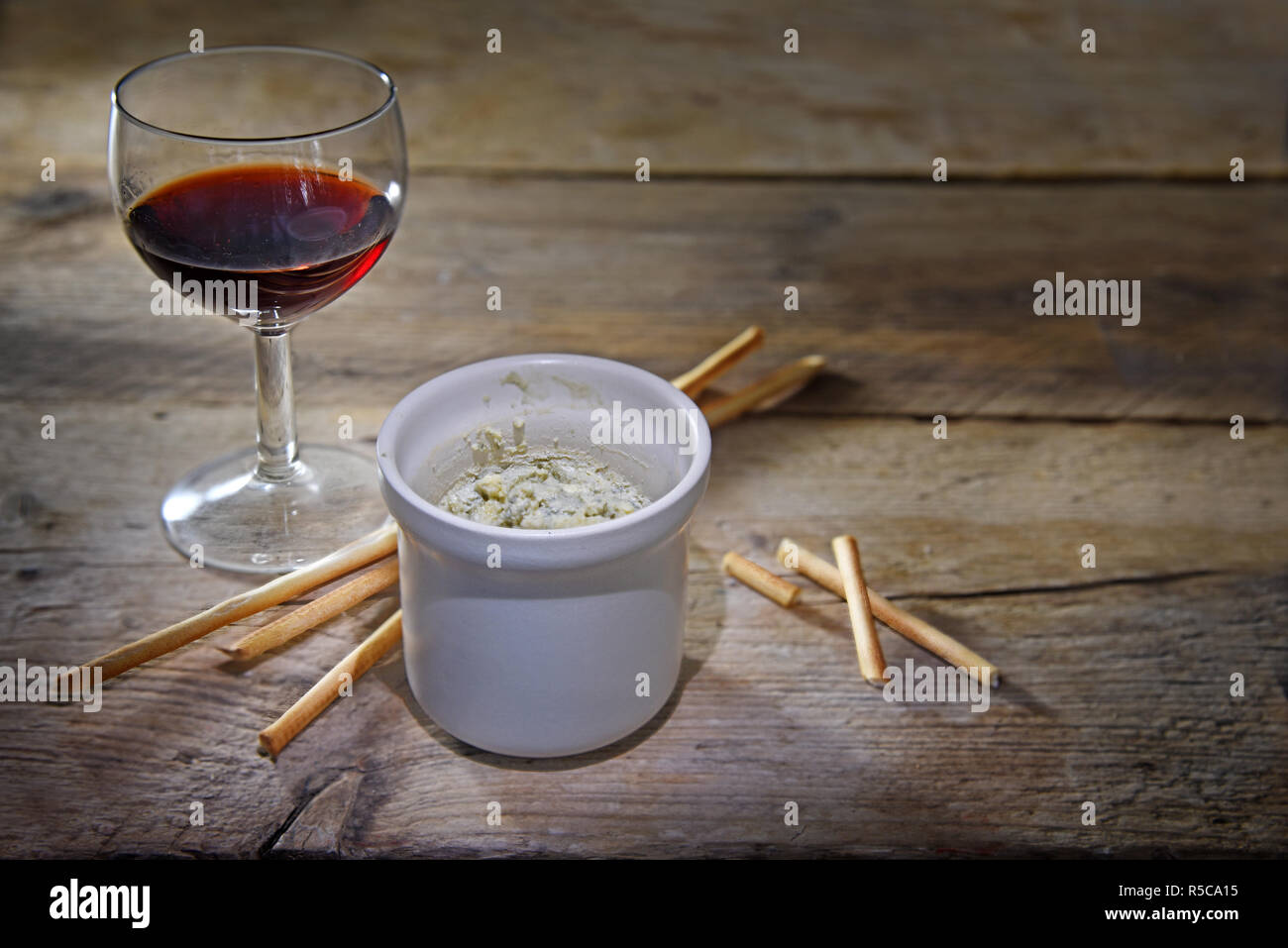 potted blue stilton cheese in a ceramic jar, port wine and some nibble sticks on a dark rustic wooden table, copy space, selected focus, narrow depth  Stock Photo